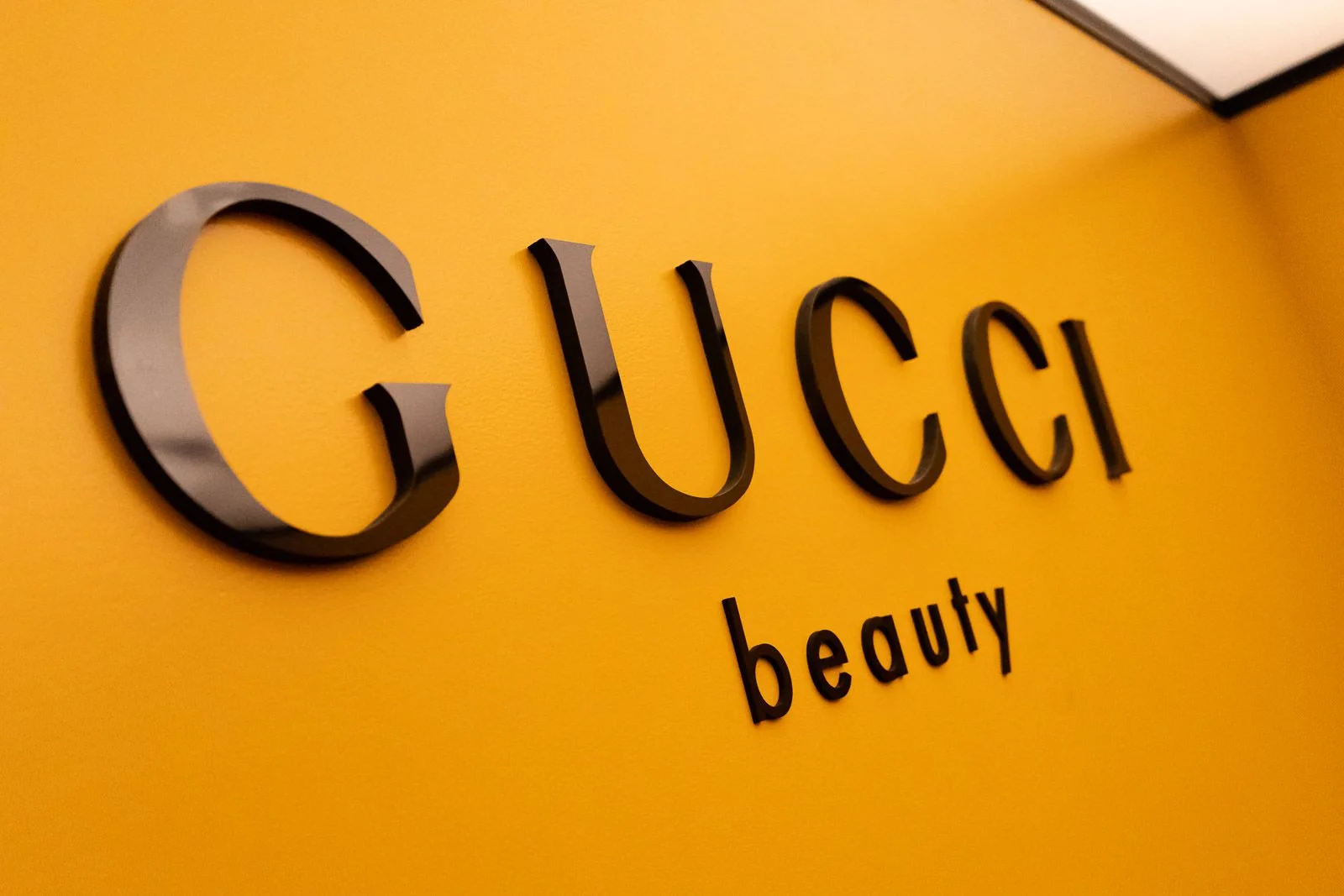 Close-up of a yellow wall with the black, three-dimensional text reading 'Gucci Beauty' and the smaller text 'beauty' underneath.