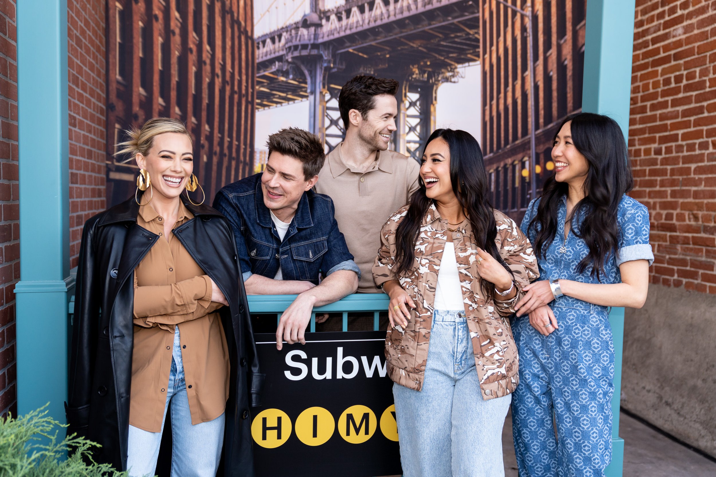 A diverse group of six friends, three women and three men, laughing and chatting while standing outdoors near a Subway restaurant sign, with a bridge in the background.  How I Met Your Father on Hulu / Disney cast.