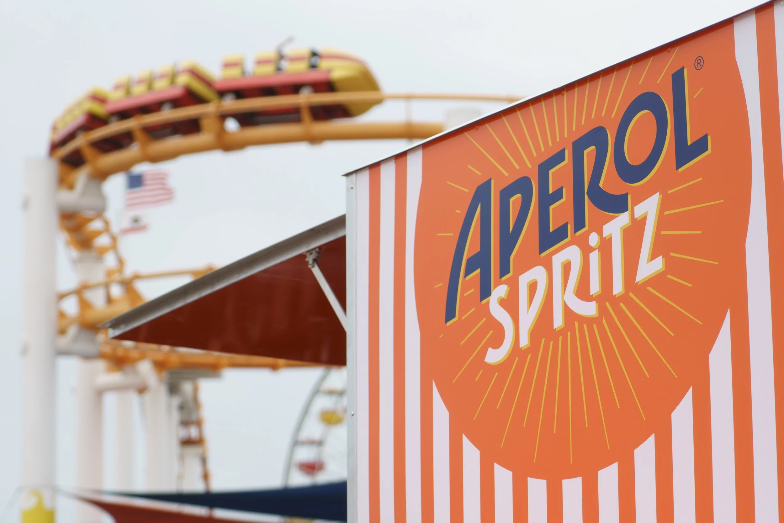 Close-up of a bright orange sign reading "Adventure Splash" with a Ferris wheel in the background at an amusement park.