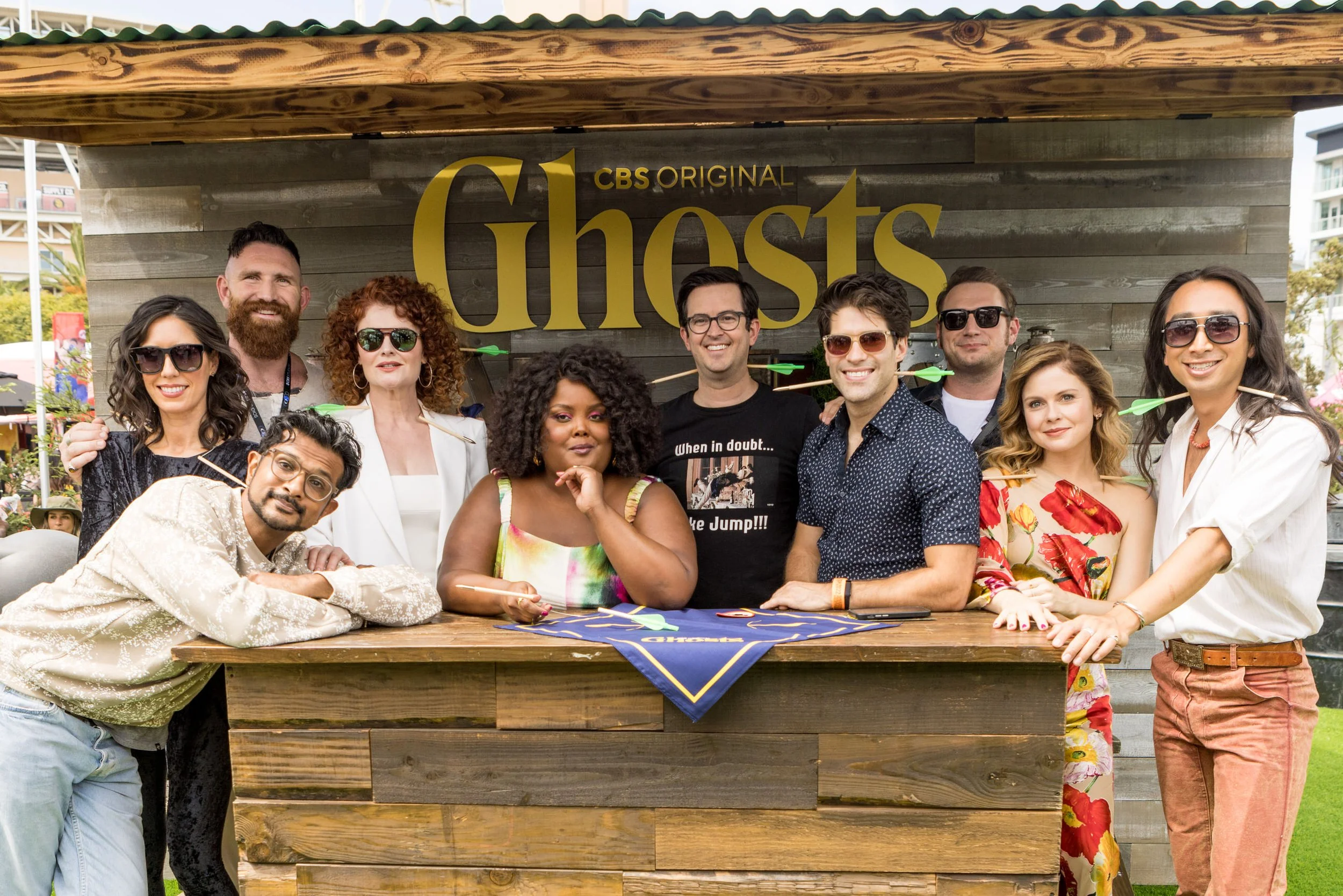 Group of people posing behind a large wooden booth with a sign that says "Ghosts" at an outdoor event.