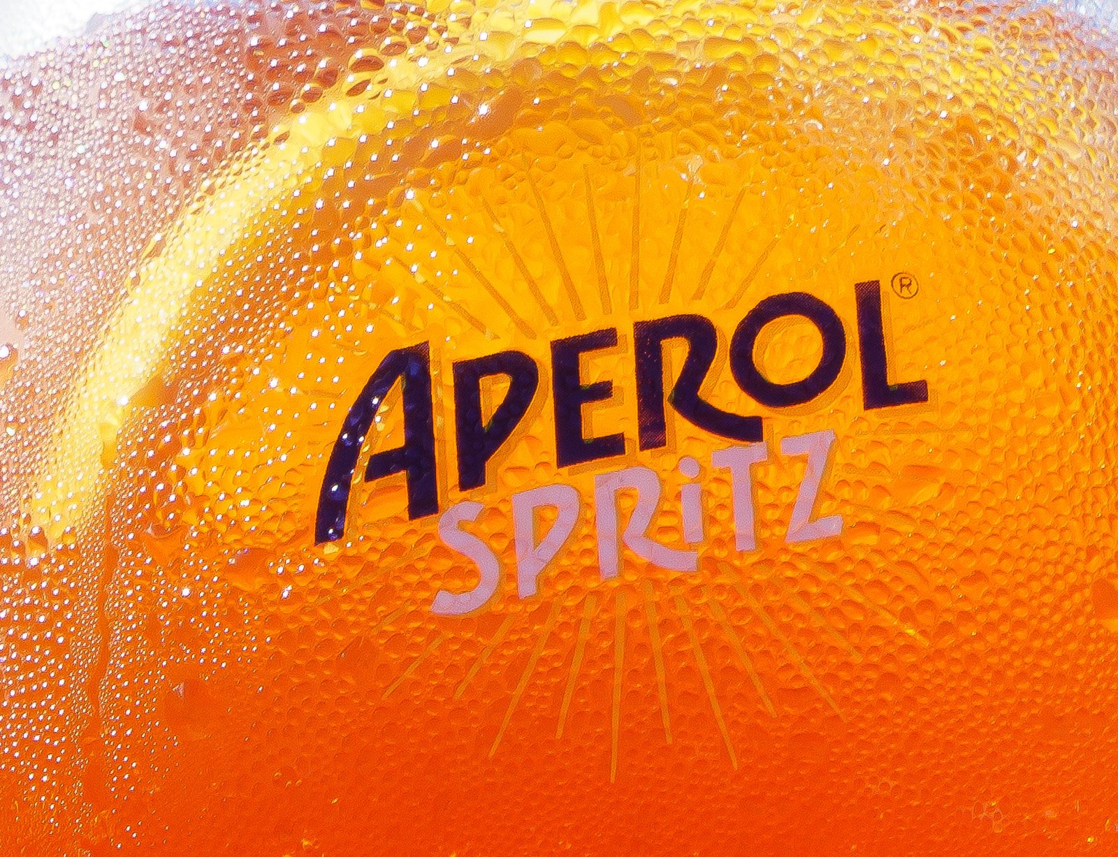 A close-up of an orange A-perol Spritz bottle with condensation, showing the brand name and logo.