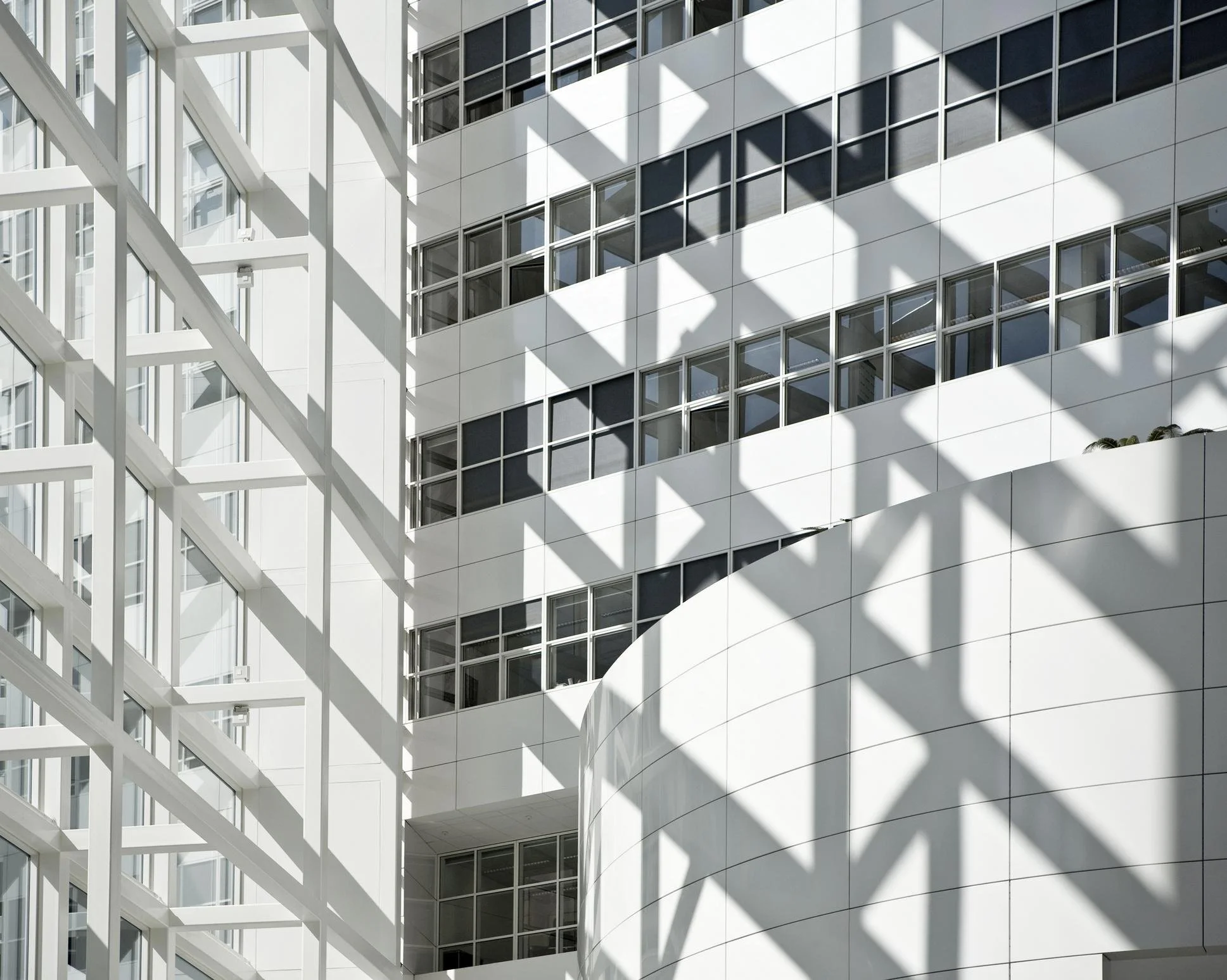 Modern white building with large windows and distinct shadows cast on its exterior, featuring an intricate metal framework.