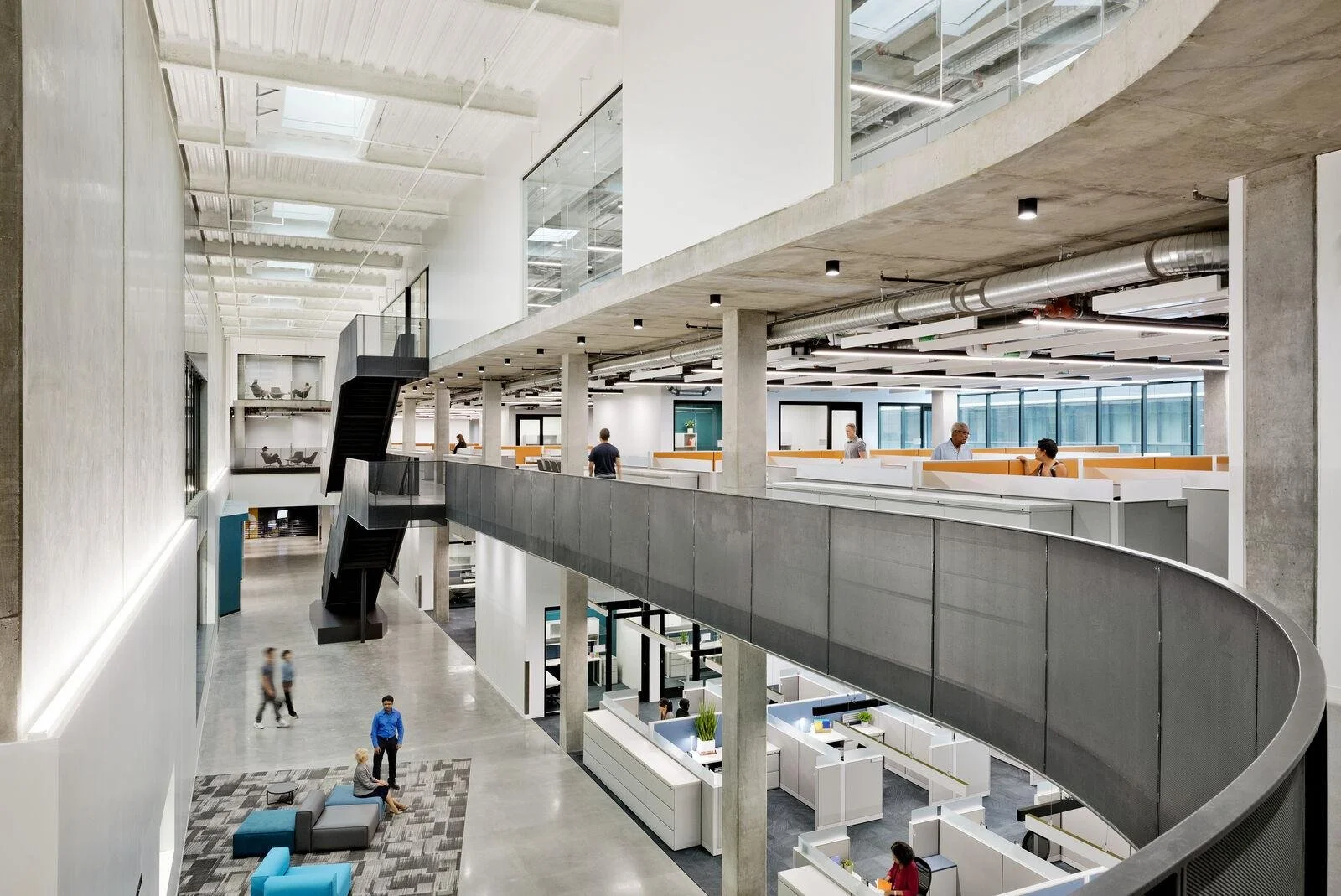 Modern office lobby with open space, multiple floors, glass walls, and people walking and working.