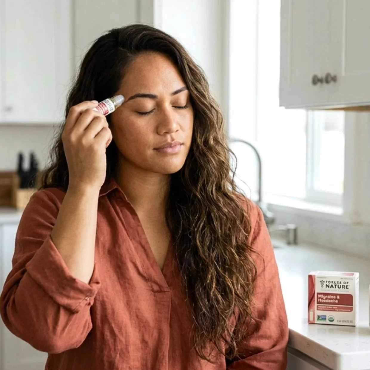 A woman with long, curly brown hair holds an allergy test kit to her forehead with her eyes closed, standing in a kitchen next to a box of migraine and headache medication.