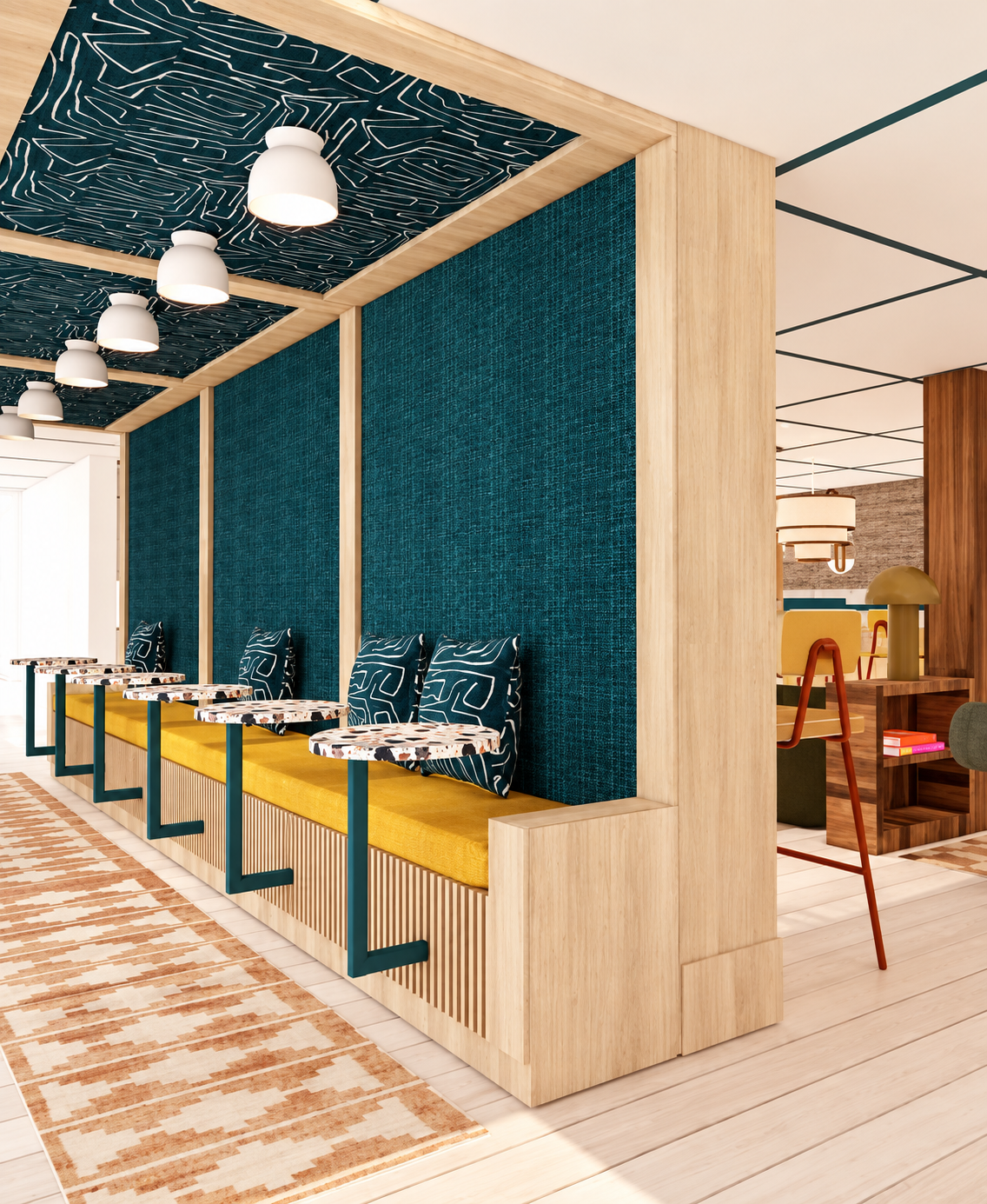 Interior of a modern hotel lobby or cafe with yellow cushioned seating, blue fabric wall covering, and decorative pillows with abstract patterns. Overhead lighting fixtures are also visible.