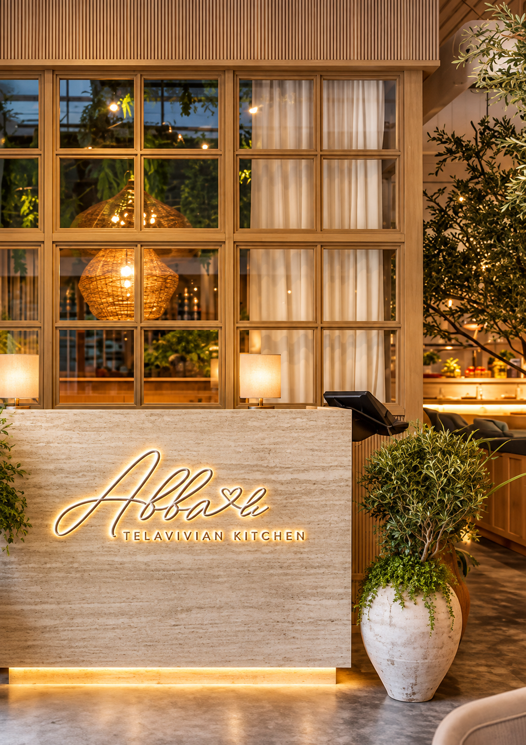 Interior view of Abxa Telavivian Kitchen restaurant with a illuminated sign, large potted plant, lighting fixtures, and decorative wooden and glass partitions.
