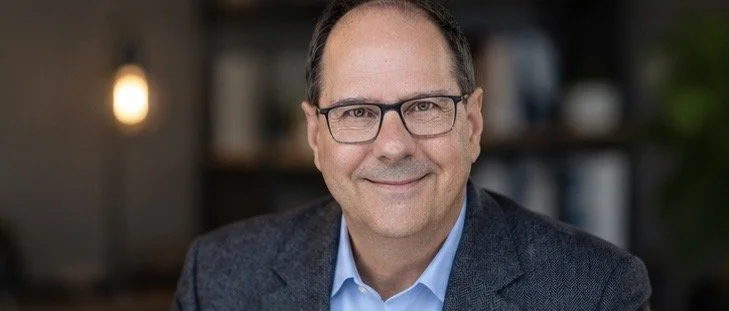 Portrait of a middle-aged man with glasses, smiling in a professional setting.