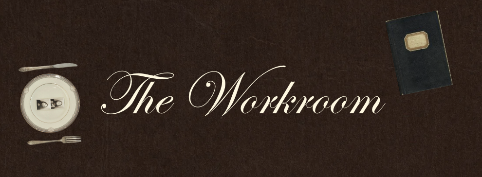 The image features a dark brown wooden surface with a small plate, a fork, a spoon, a closed black book, and the words 'The Workroom' written in elegant cursive font.