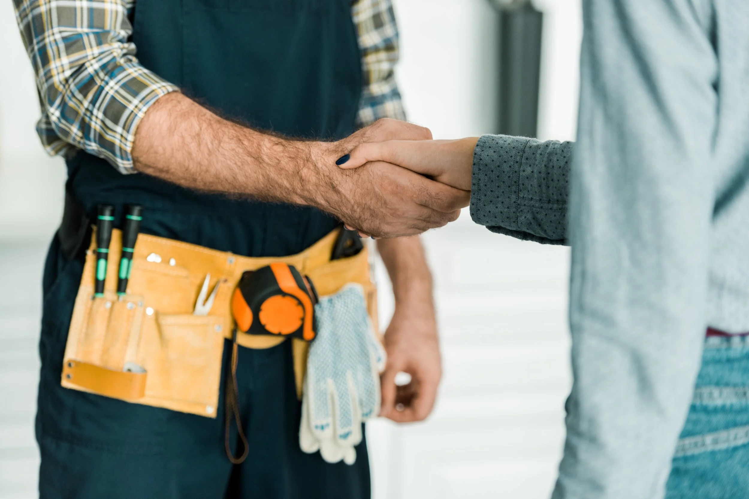 Two people shaking hands, one with a construction tool belt, indicating a professional setting or agreement.