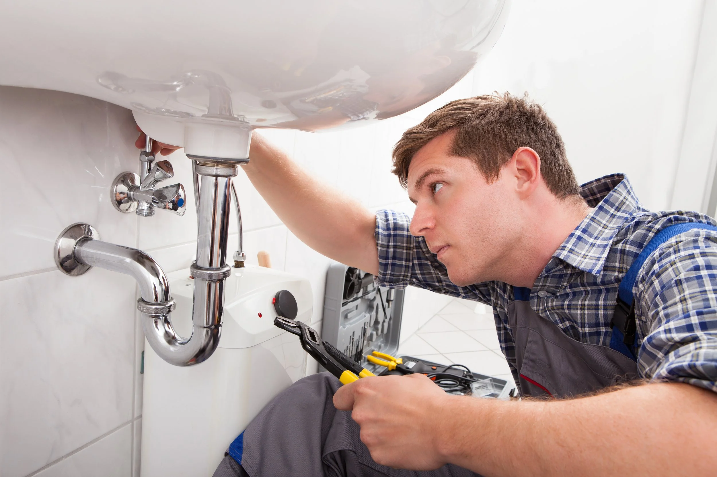 A technician working on plumbing under a sink, using tools to fix or install pipes.