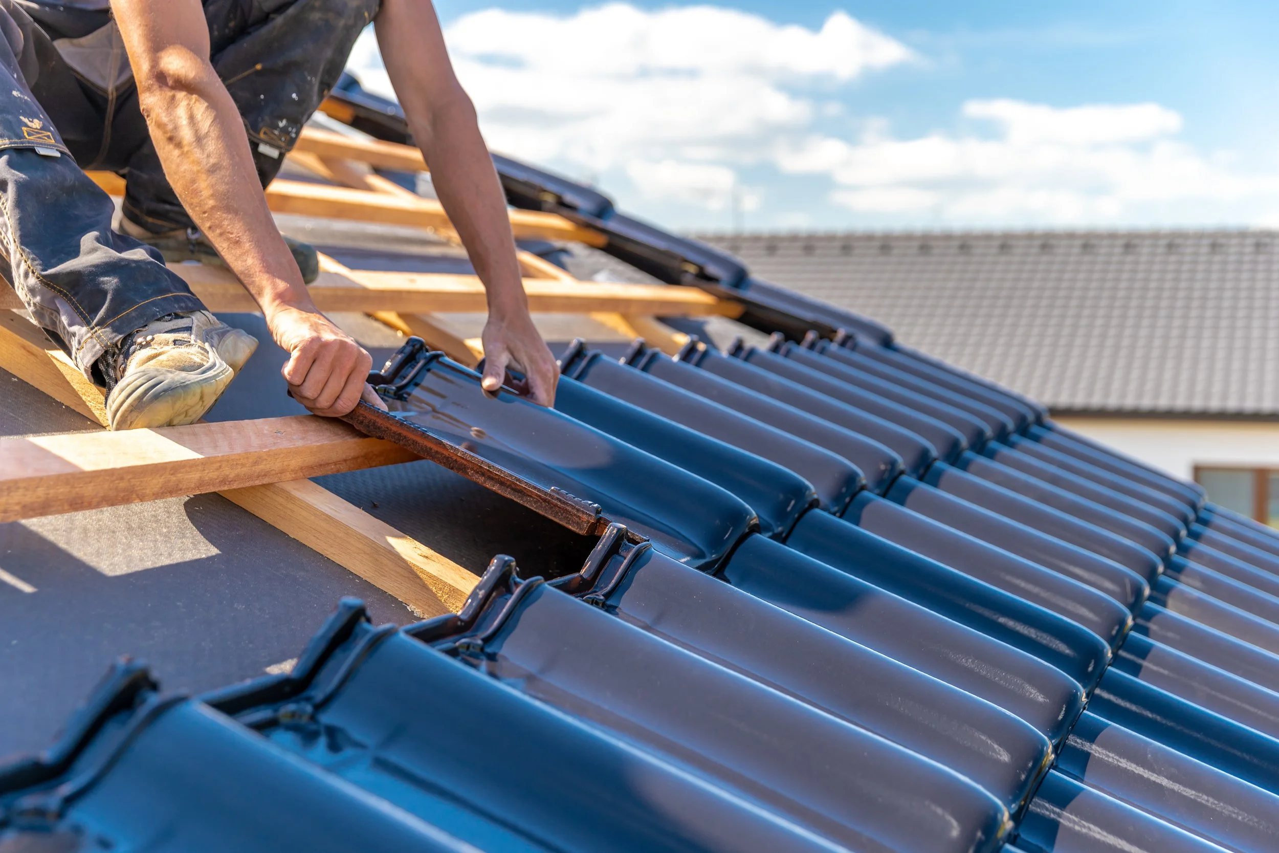 Person installing solar roof tiles on a sloped roof during daytime, with a clear sky in the background.