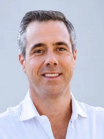 A man with short gray hair, who is a member of the Clube Pickleball Lisboa Board, smiling, wearing a white button-up shirt, against a light blue background.