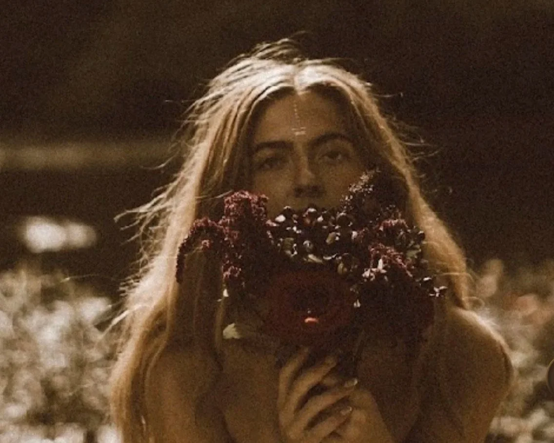 A woman with long hair holding a large bouquet of dark purple flowers in front of her face at night.