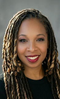 Portrait of a woman with long dreadlocks, smiling, wearing a black top.
