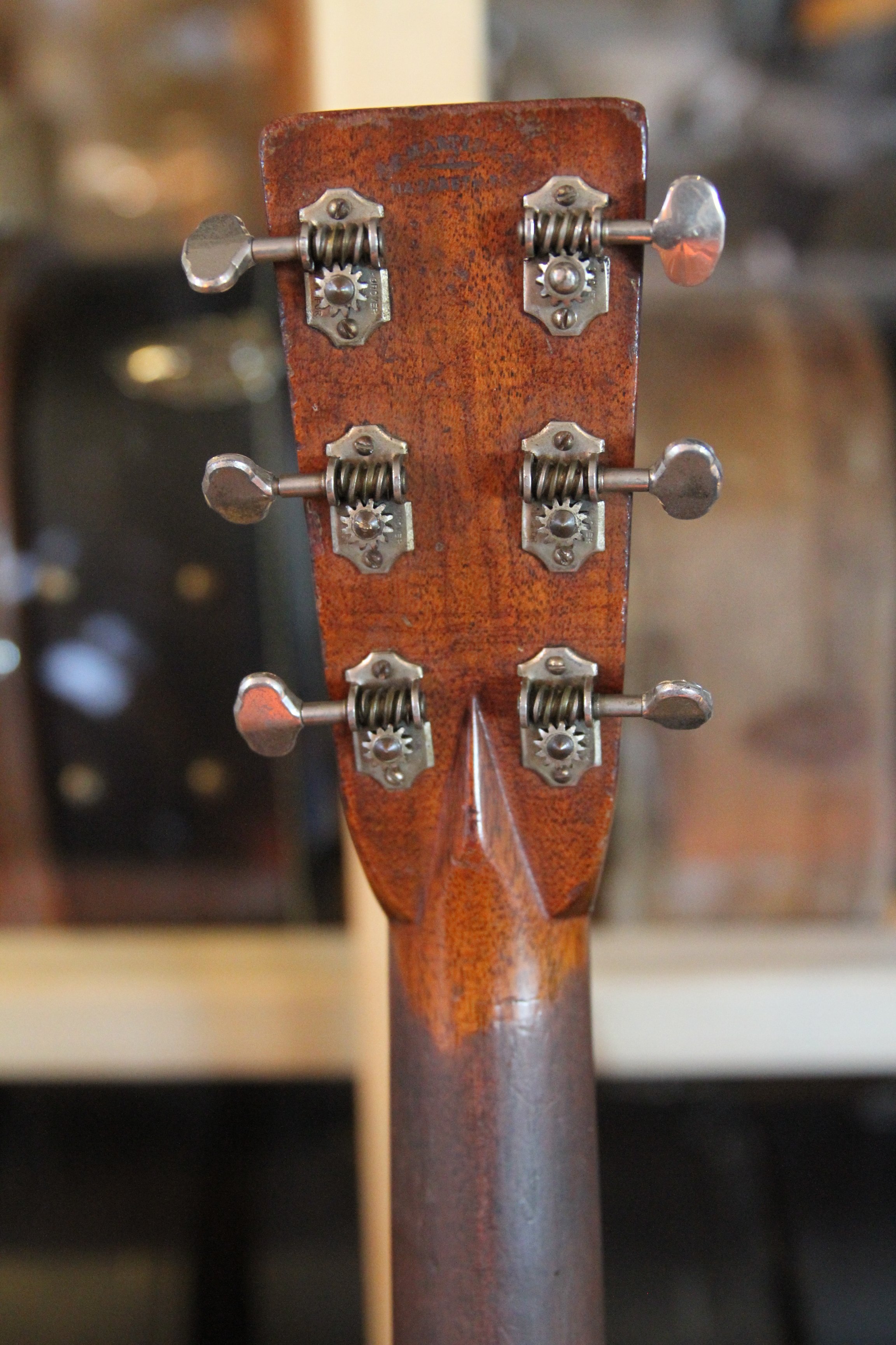 Close-up of the back of a vintage wooden guitar headstock with tuning pegs, gears and worn neck .