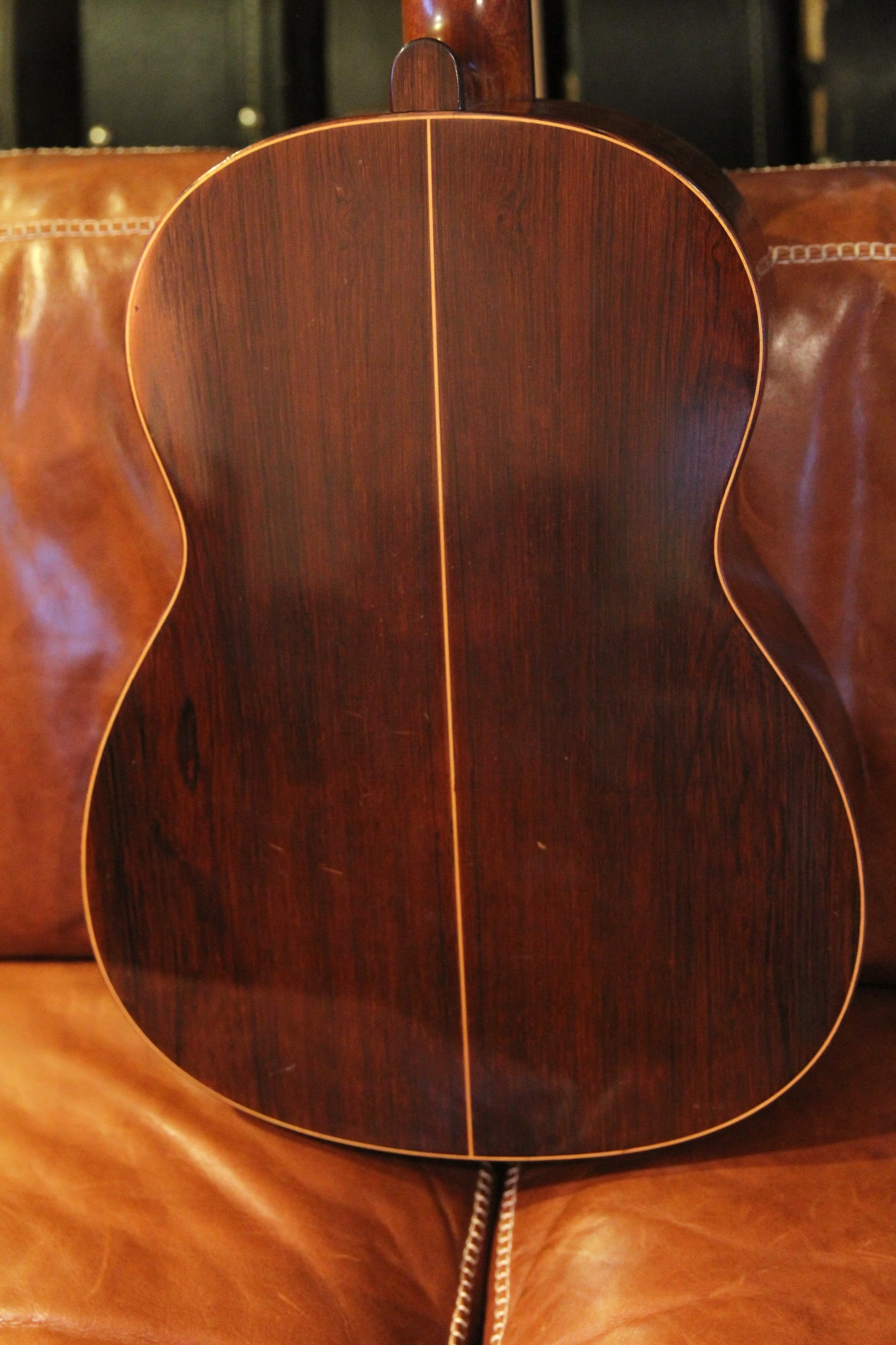 Close-up of the back of a wooden acoustic guitar resting on a leather surface