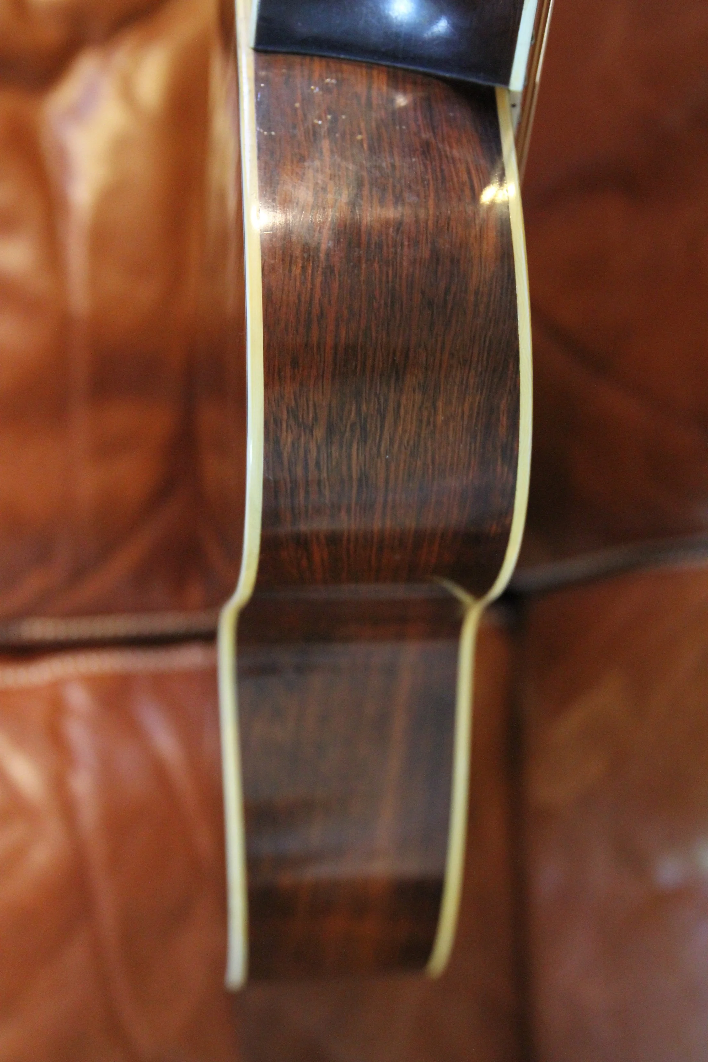 Close-up of an acoustic guitar's bass side, showing wood grain and whitw binding.