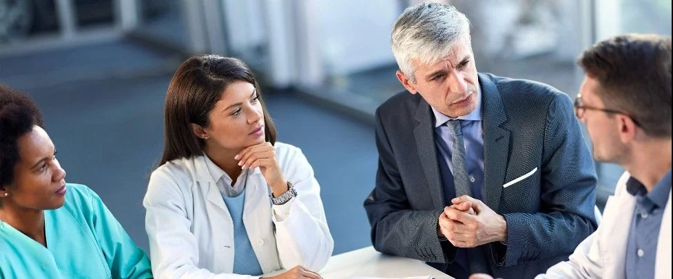 A group of four diverse medical professionals having a serious discussion in a hospital setting.