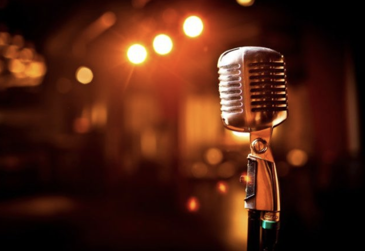 A vintage microphone on a stand with stage lights in the background, likely in a performance setting.
