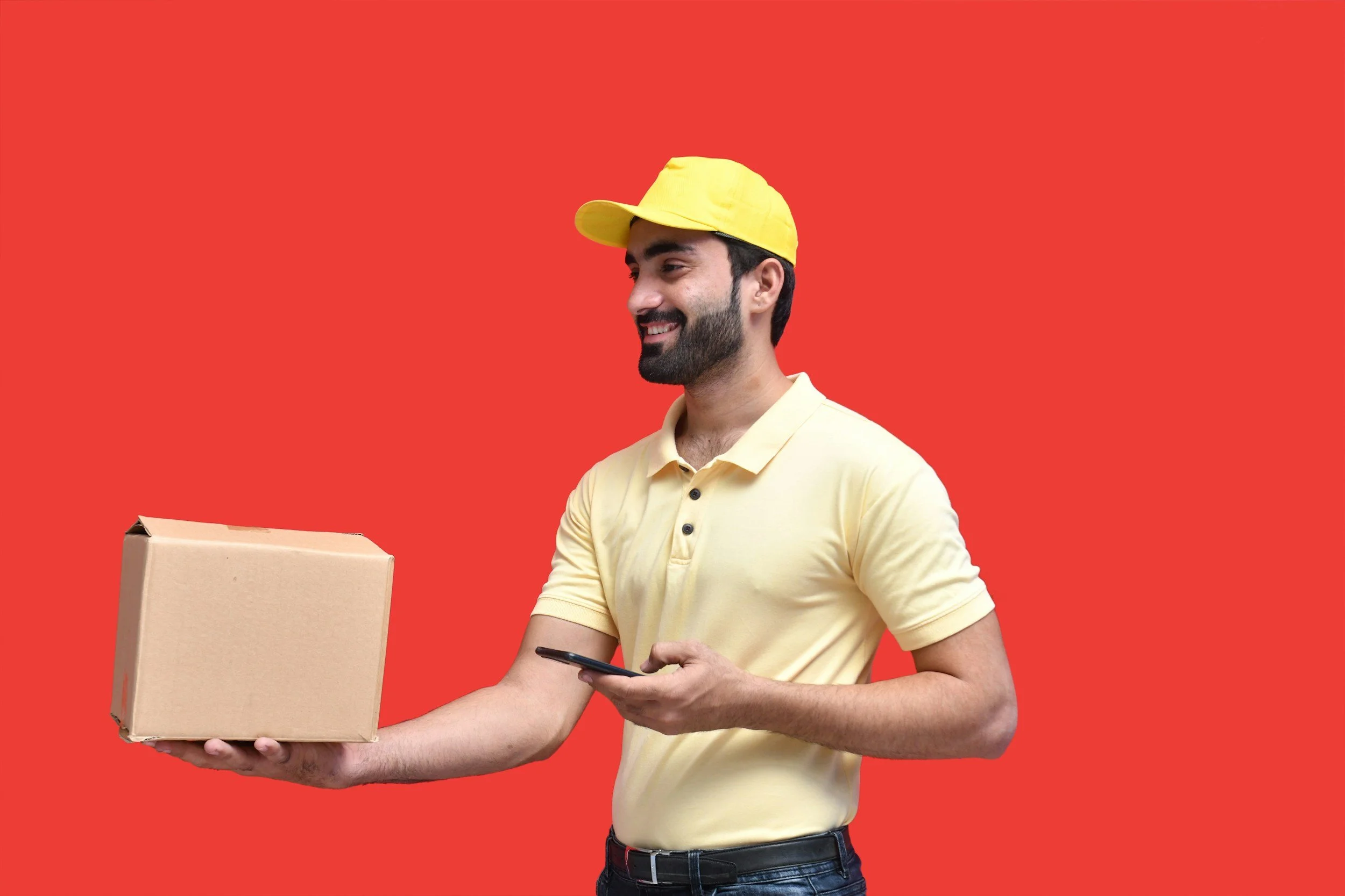 A man holding a cardboard box and looking at his phone against a red background.