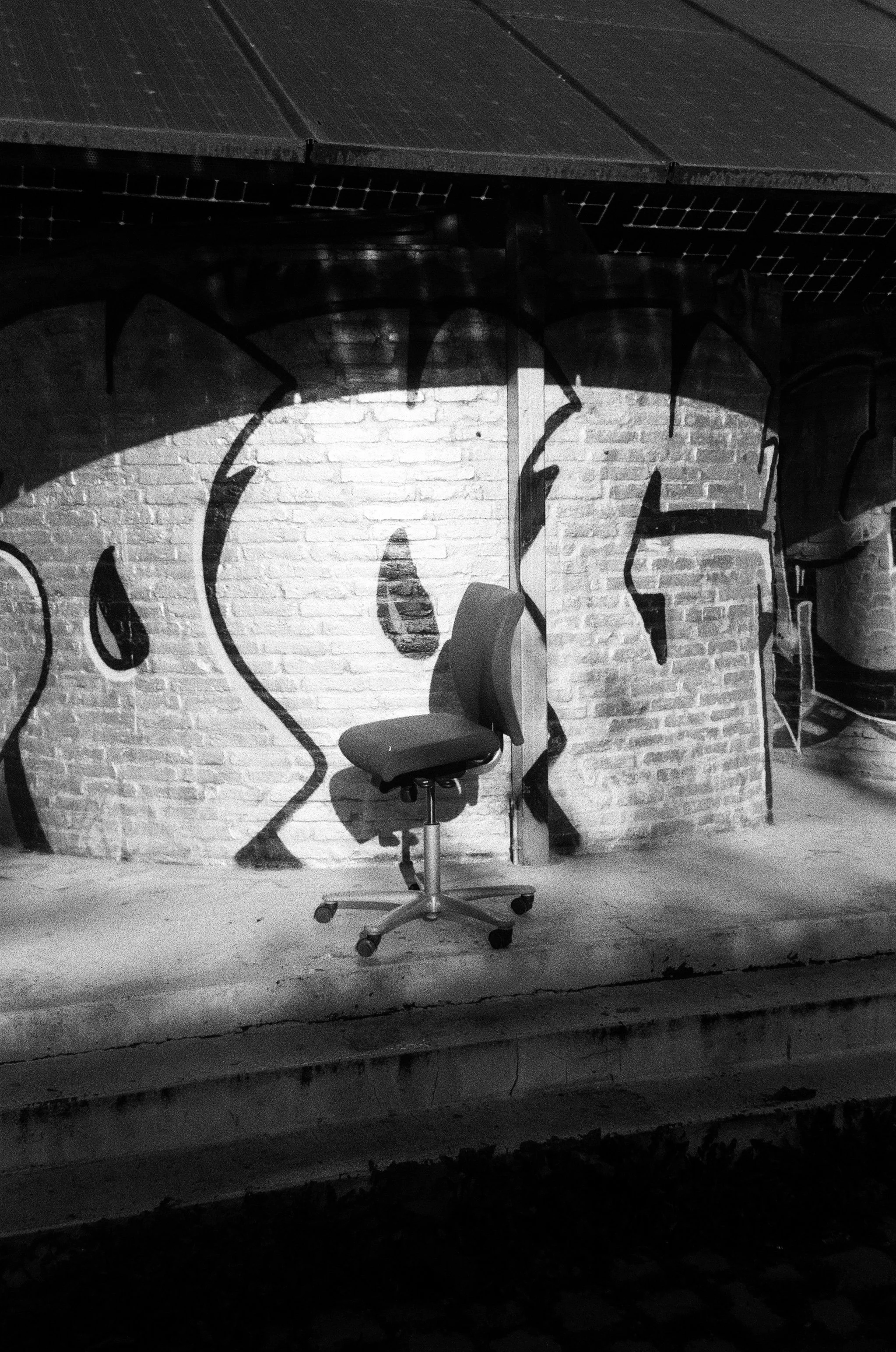 Sedia da ufficio in un ambiente industriale con parete in mattoni decorata con murale di un volto, foto in bianco e nero.
