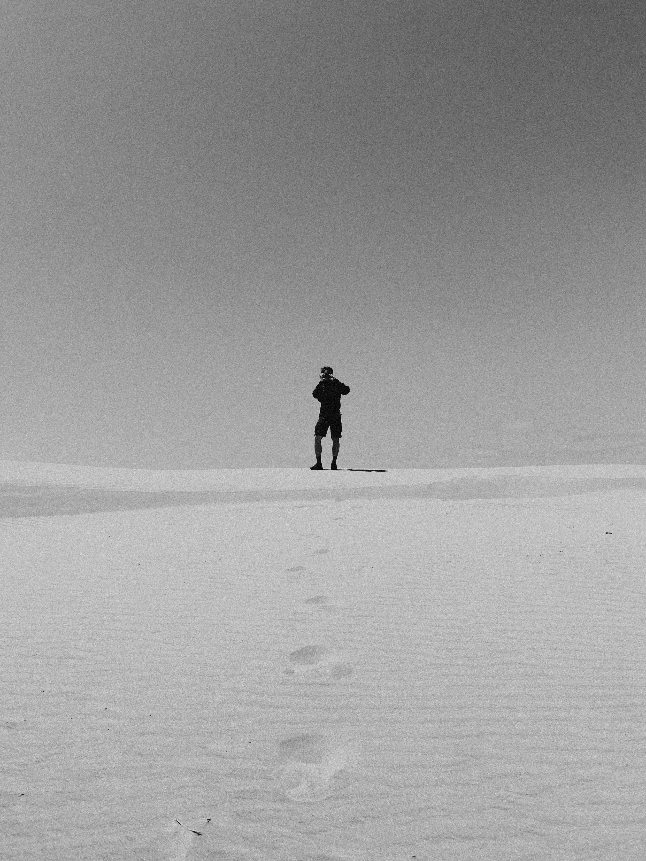 Uomo che si utilizza una macchina fotografica in un paesaggio desertico o di neve, con un cielo aperto sopra di lui.