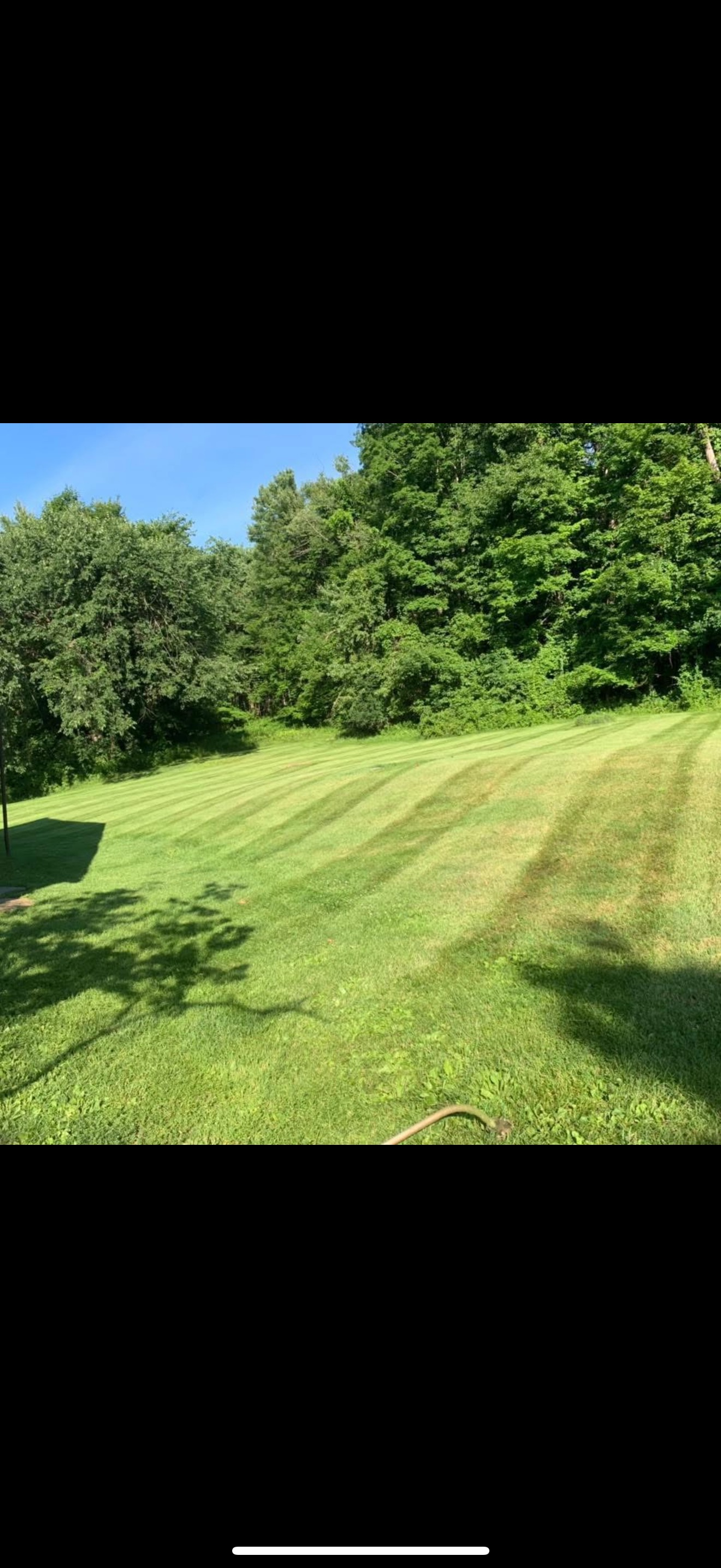 A golf course with freshly mowed green grass, surrounded by trees and shadows on the ground, under a bright blue sky.