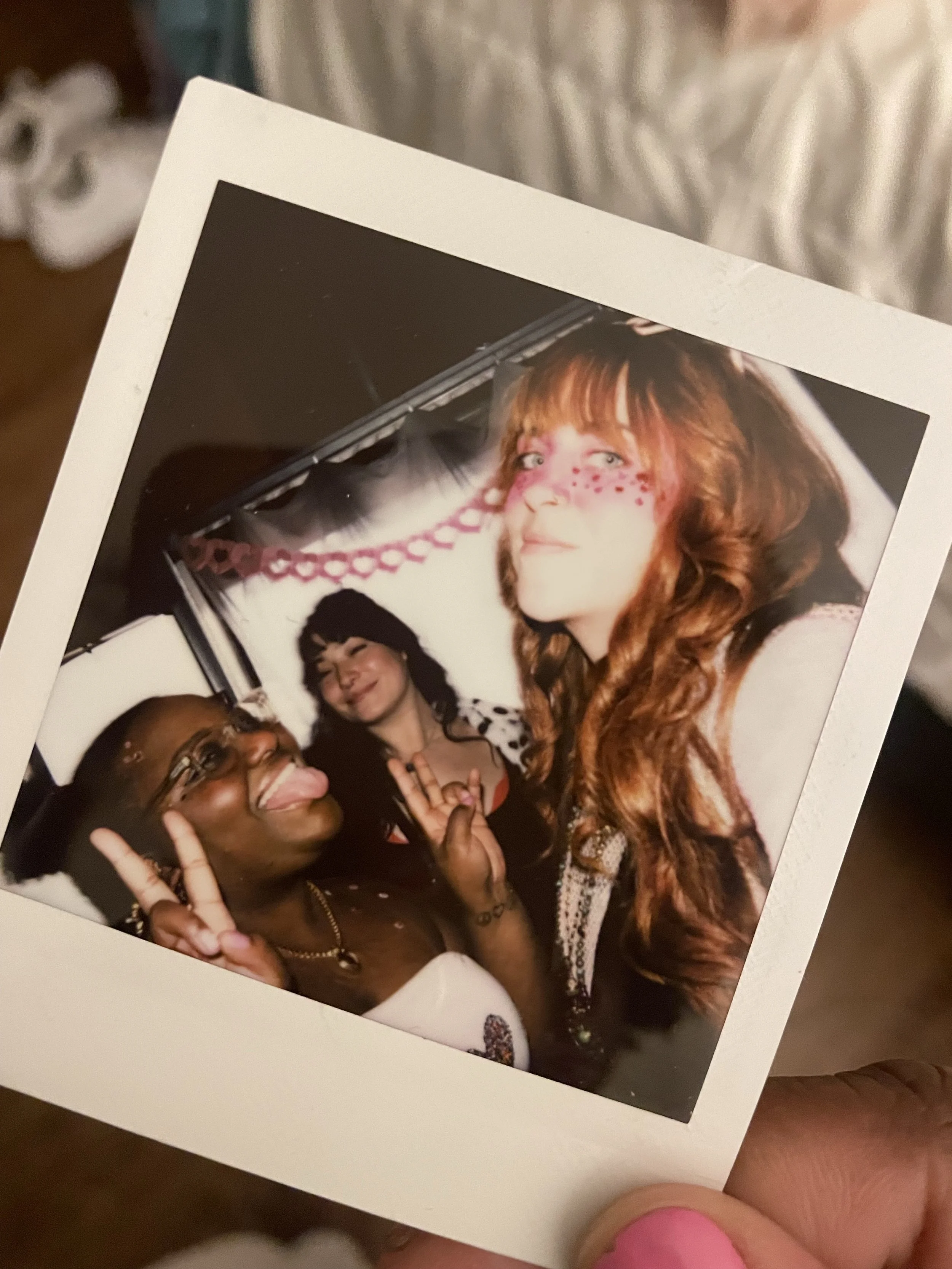 Framed group photo of three friends posing together, including a red-haired person with face paint and a person making a peace sign.