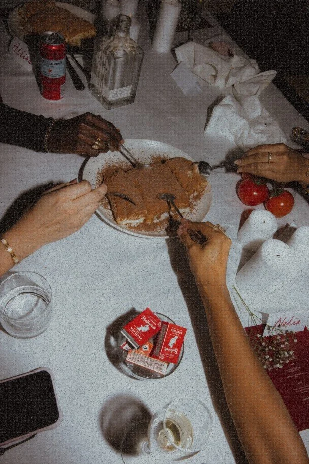 Group of diners carving a roast chicken at a restaurant table with tomatoes, wine, and utensils.