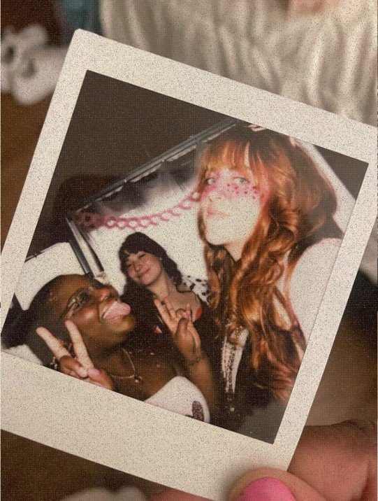 Vintage Polaroid photo of three friends posing together at a party, with one person wearing butterfly face paint and another flashing a peace sign