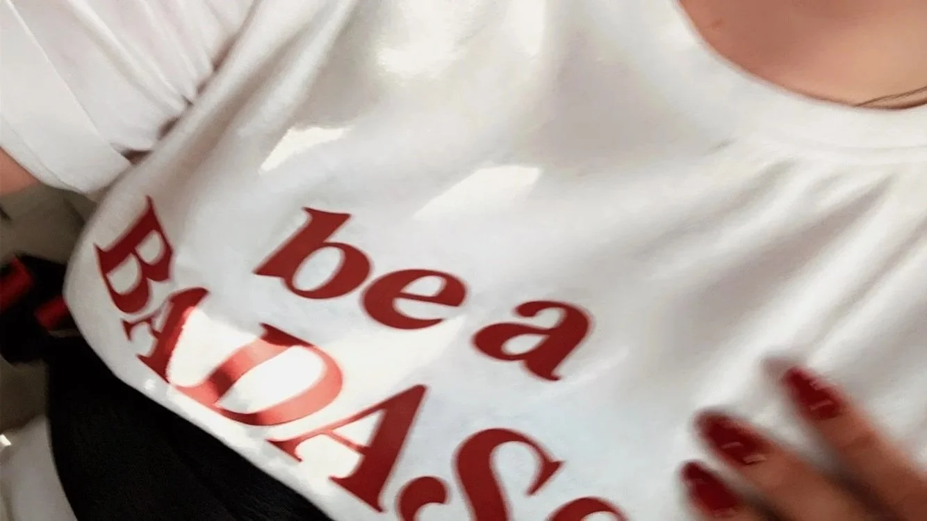 Close-up of a person wearing a badass white T-shirt with large red lettering and red-painted fingernails.
