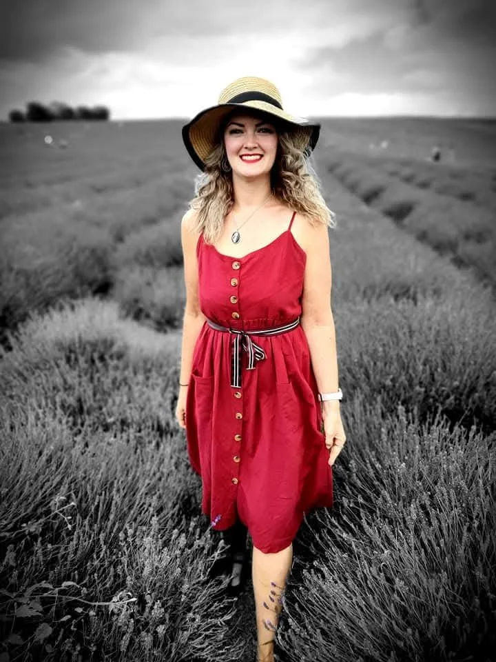 Shara in straw hat standing in a field of gray-toned wildflowers.
