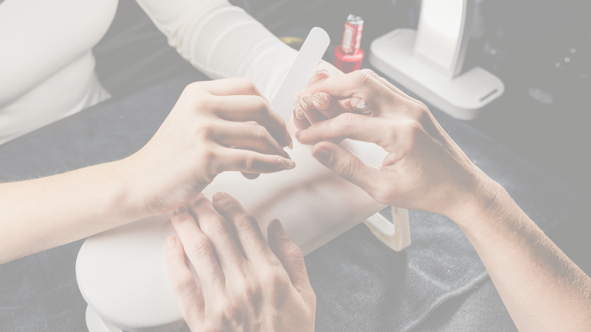 Close-up of a person receiving a manicure at a nail salon, with nail tools and nail polish in the background.