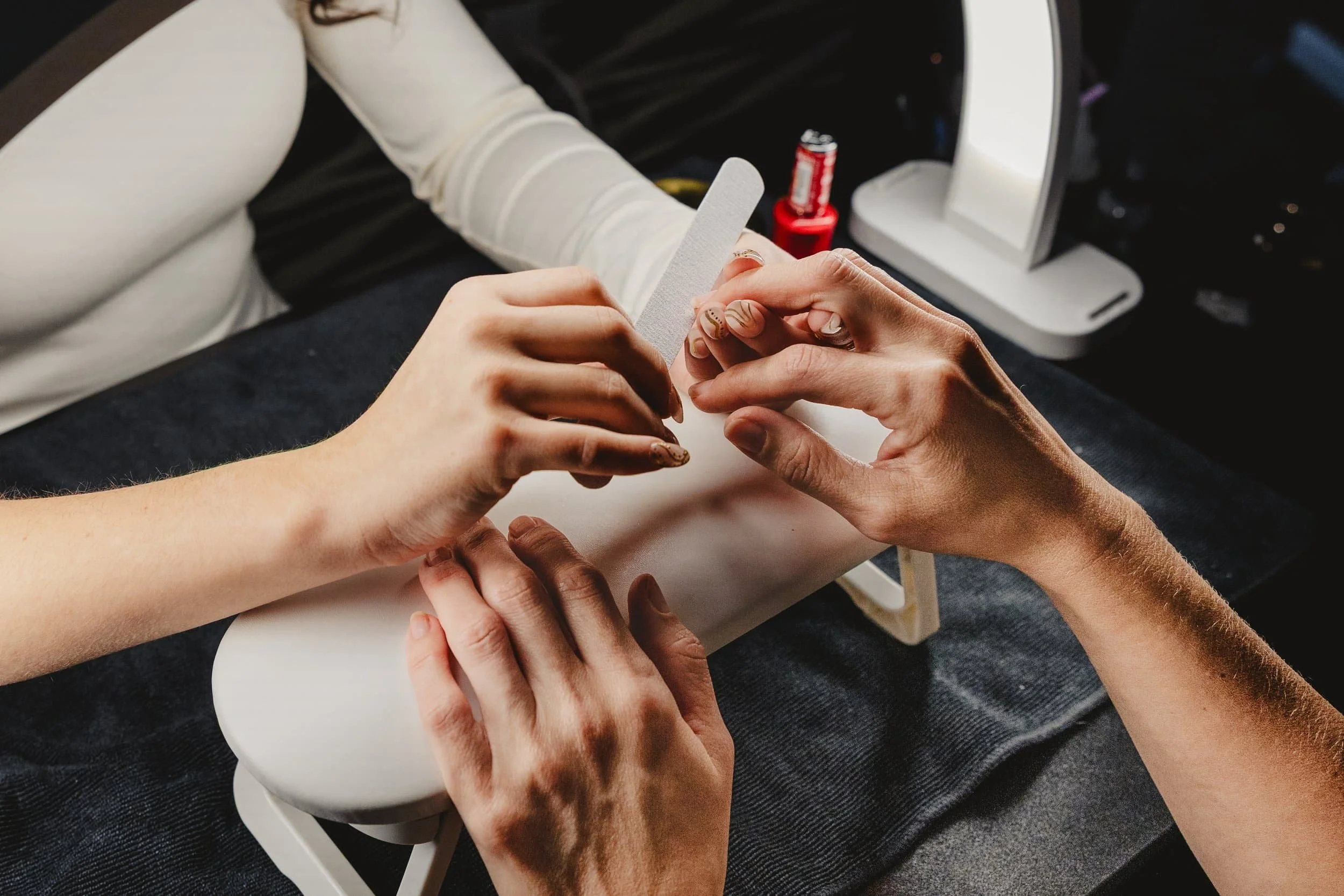 Close-up of a person receiving a manicure, with hands holding a nail file and another person shaping their nails.