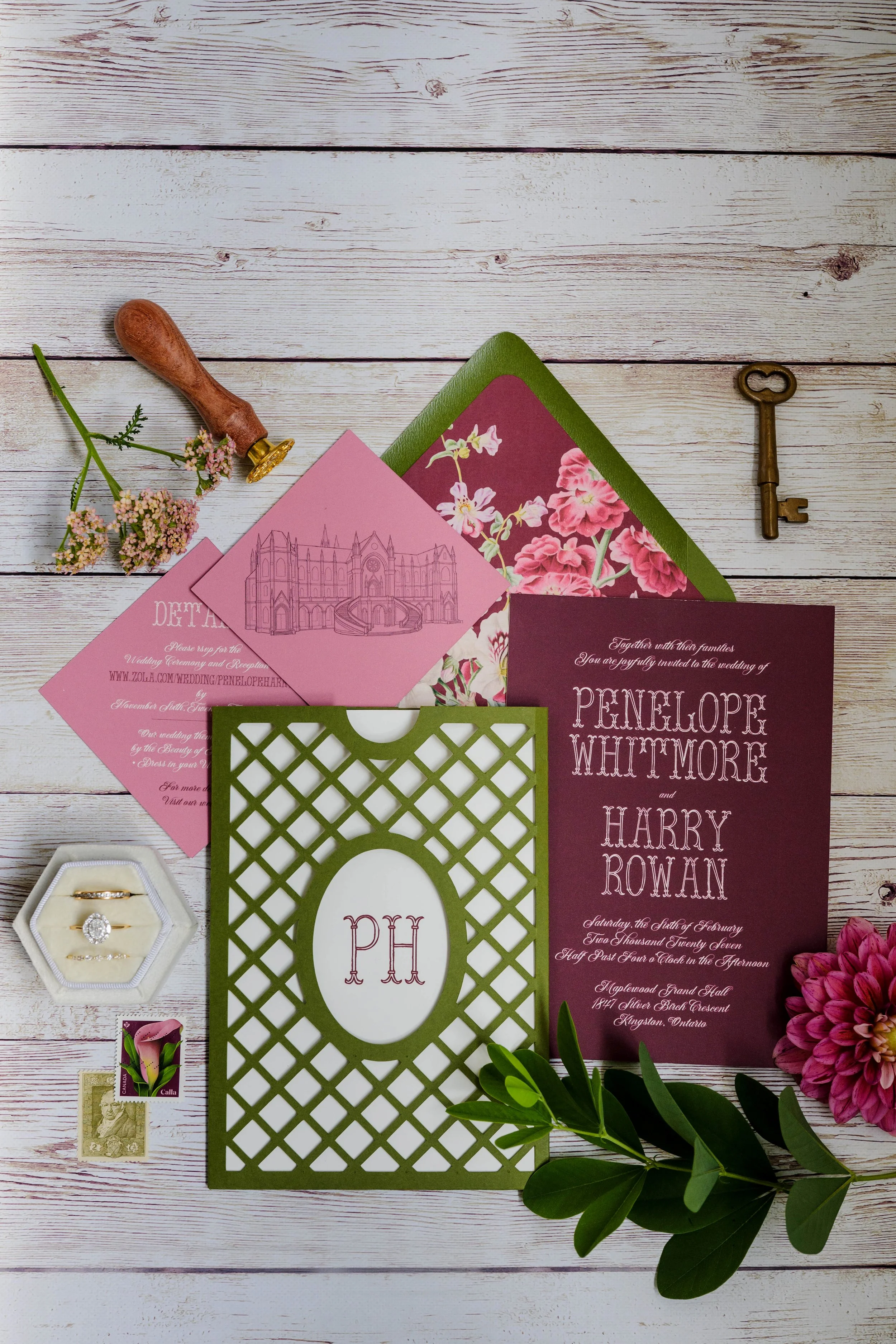 Wedding invitation, floral arrangements, jewelry, stamps, and decorative paper on a white wooden surface.
