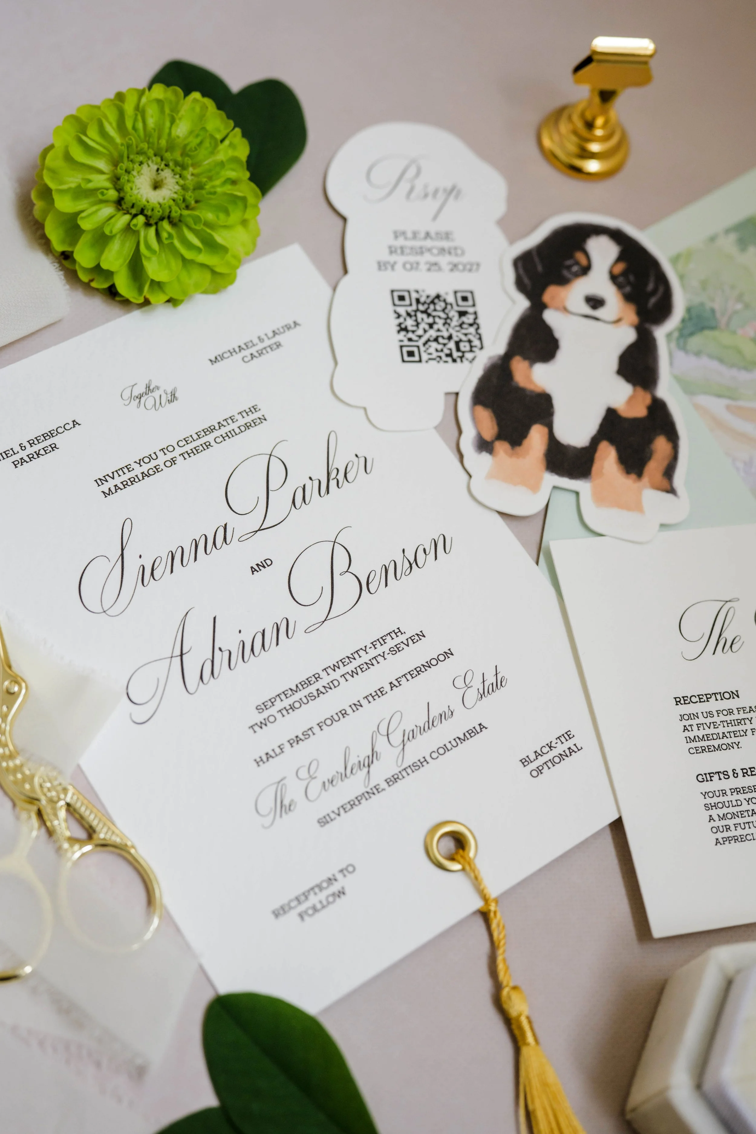 Close-up of a wedding invitation with elegant cursive and serif fonts, a green flower, a small dog illustration, a gold and a yellow tassel, and a gold paper clip on a beige background.