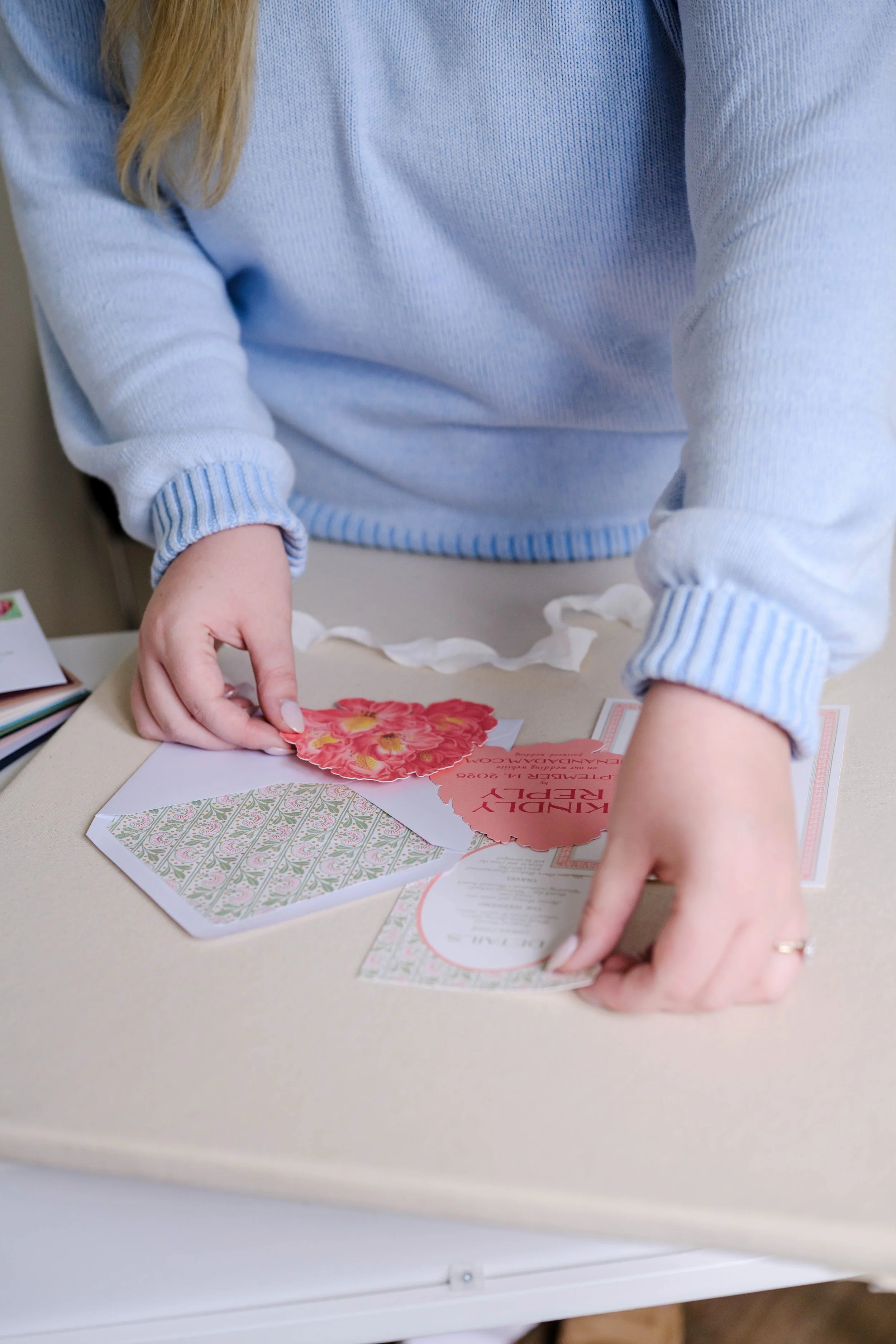Person arranging wedding or event invitations and decorative paper on a table.