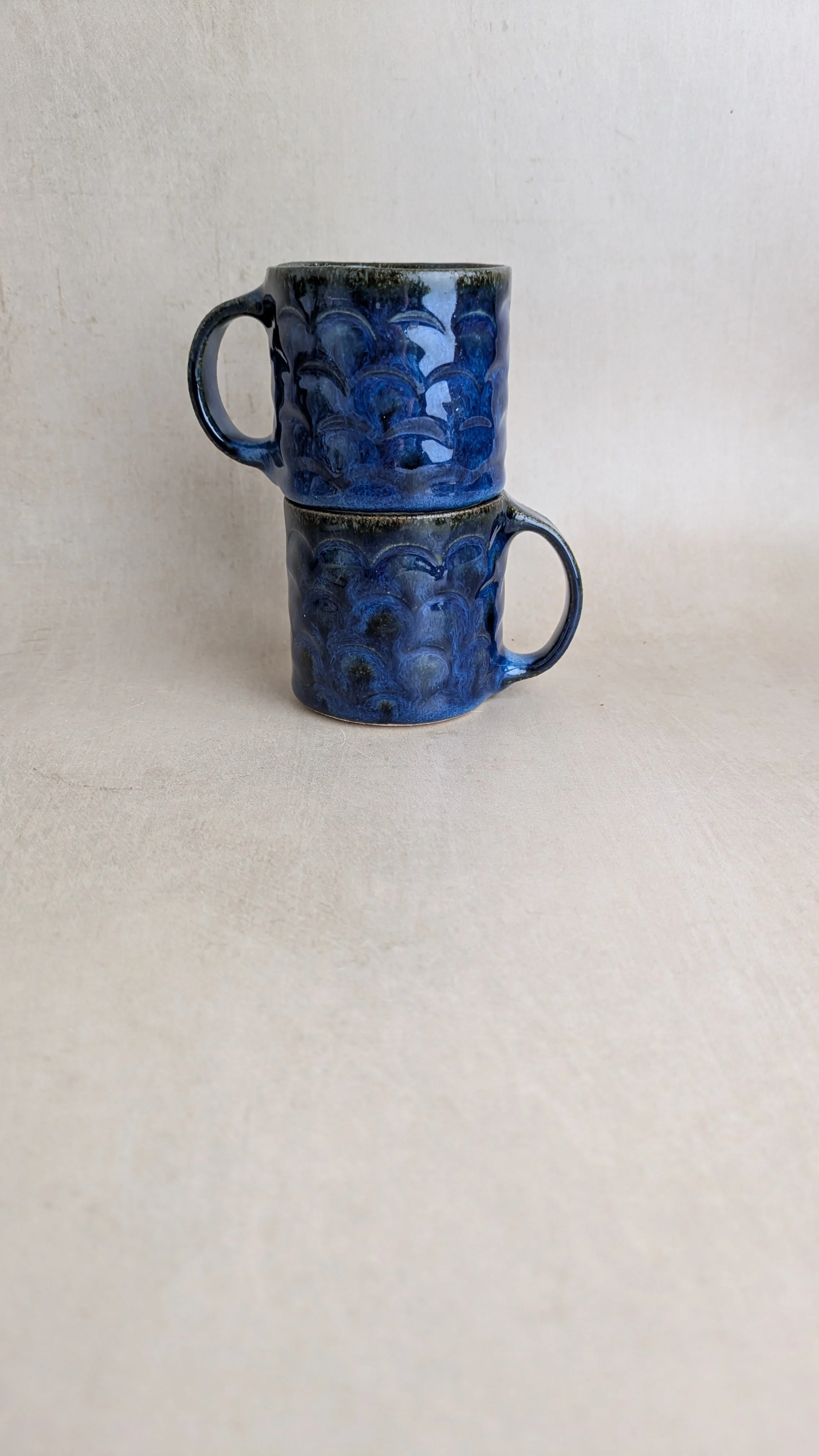 Two Azul Lazuli mugs stacked vertically, highlighting their rich blue glaze and arch texture.