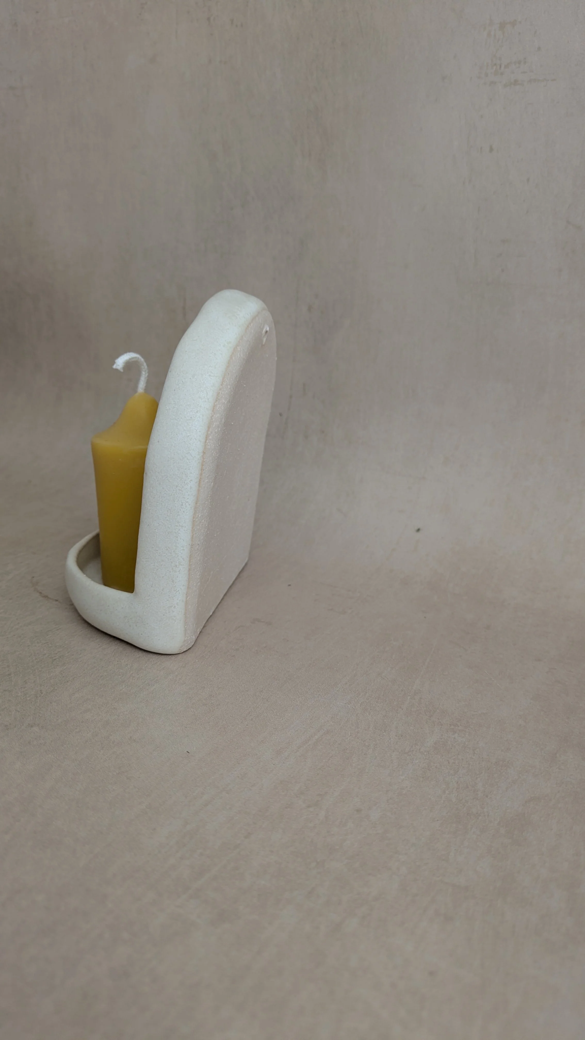 Side view of cream ceramic wall sconce showing curved back and beeswax candle placement.