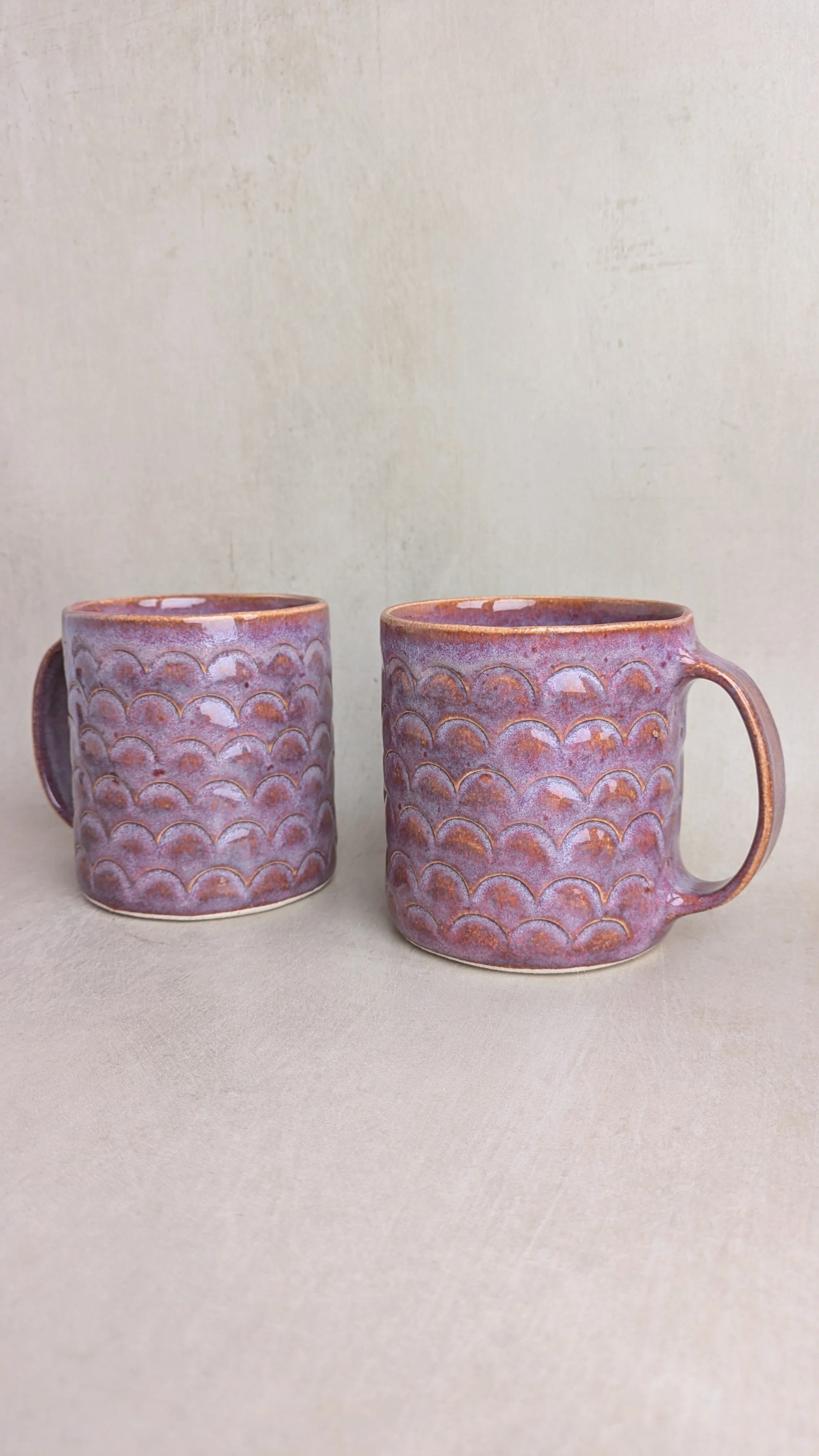 Two large purple arch mugs with textured scalloped pattern, side by side on a neutral background.