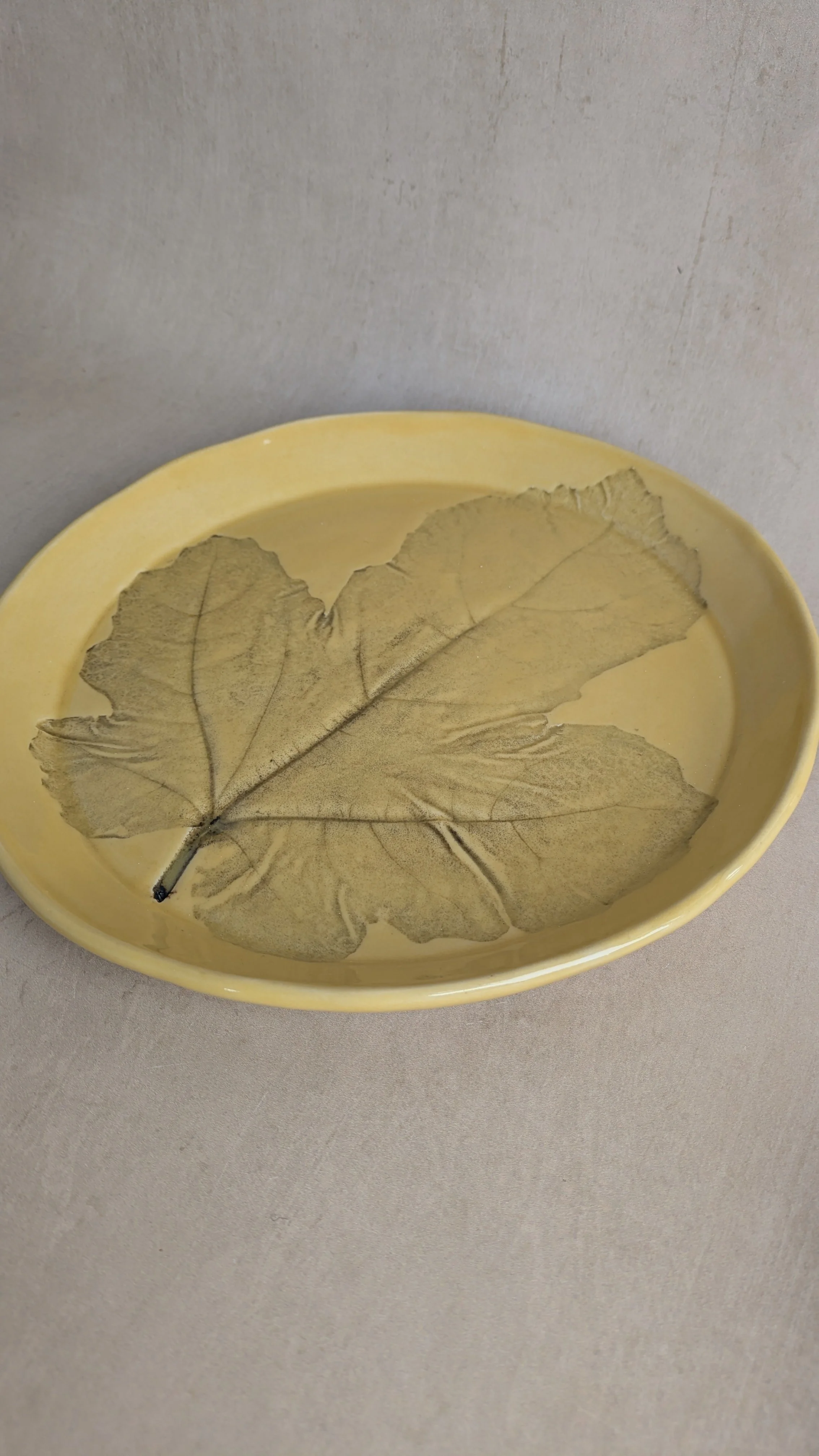 Stoneware plate with fig‑leaf impression in soft yellow glaze, minimal styling.