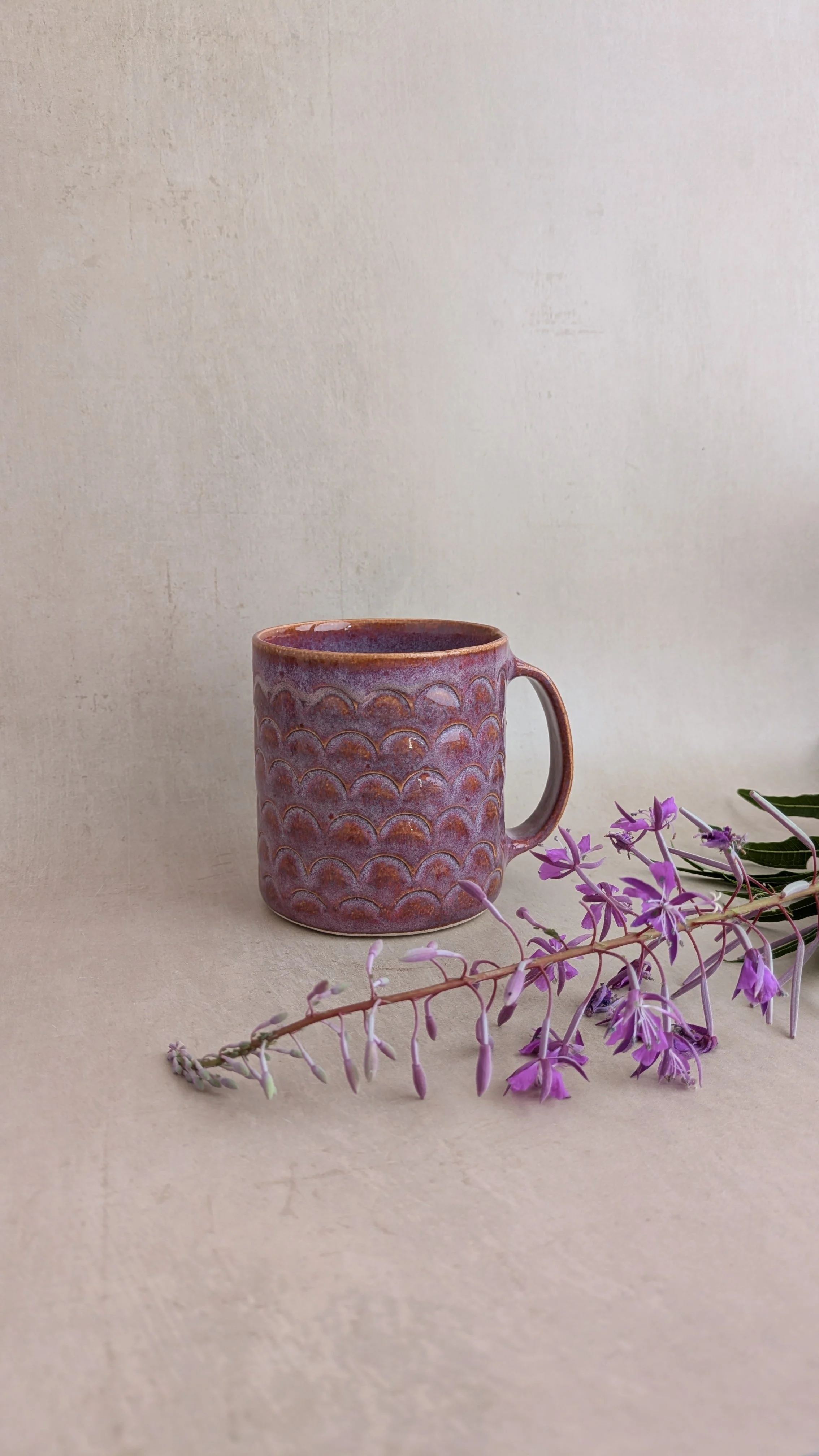 Purple arch mug beside a cut fireweed stem lying on a beige surface.
