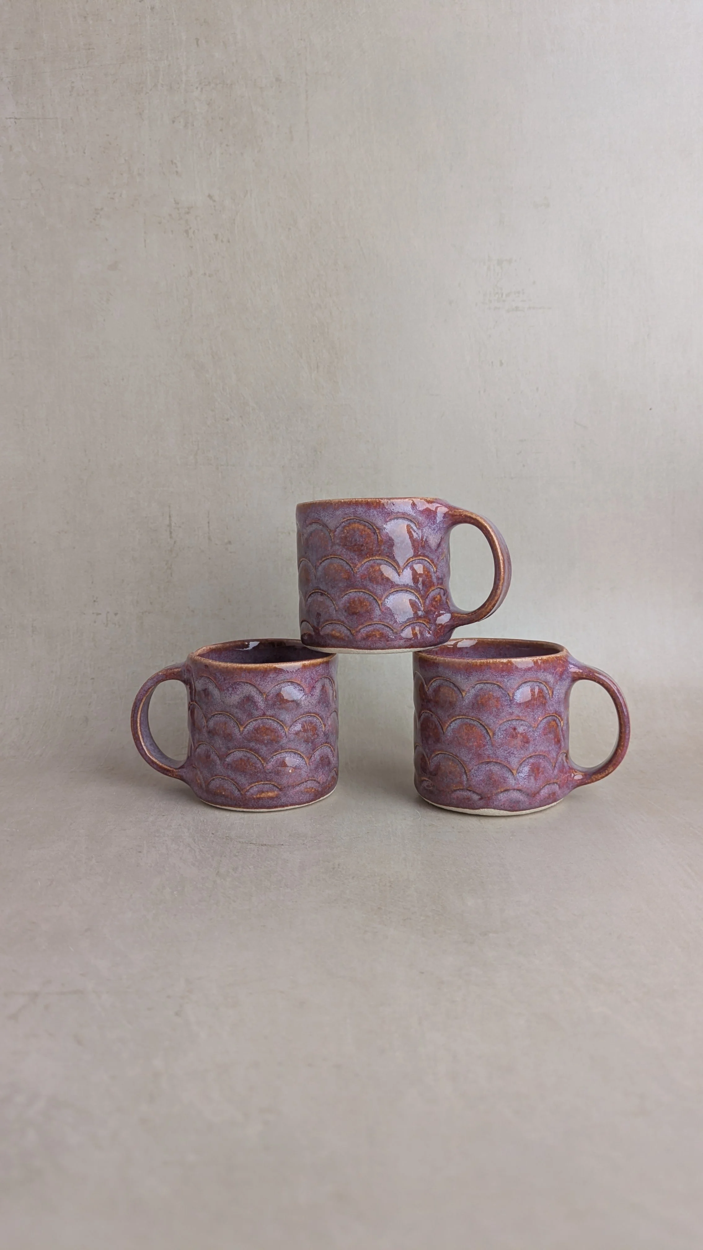 hree small purple mugs stacked in a pyramid formation, showing their scalloped texture and glossy glaze.