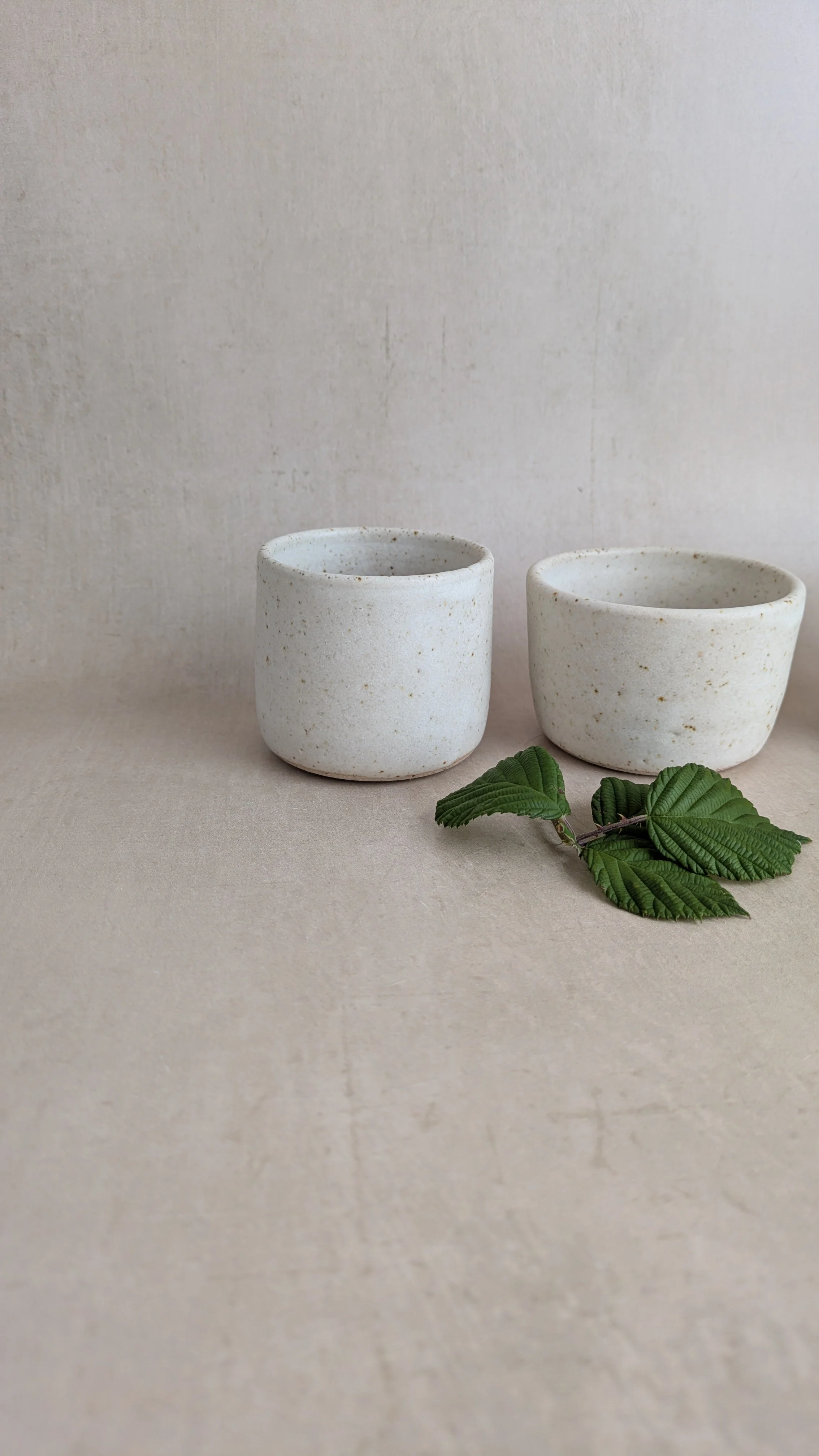 Two handmade cream speckled pottery condiment pots with green leaves.