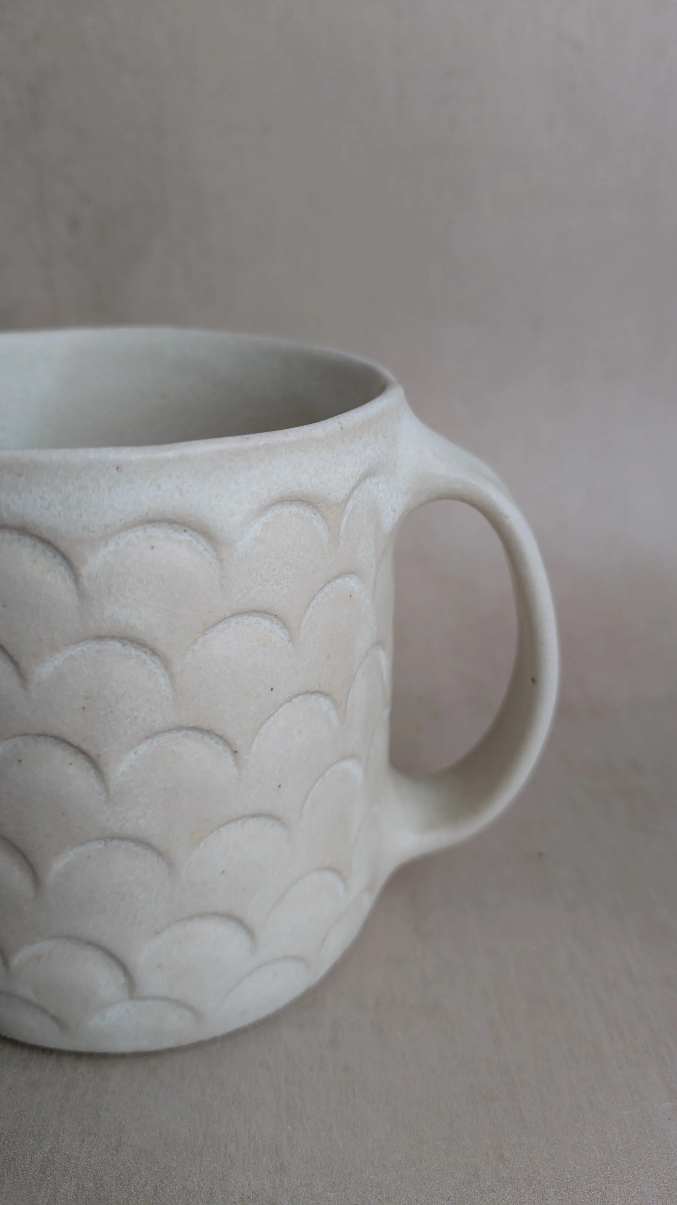 Detailed view of ceramic mug handle and scallop pattern texture in soft natural light.