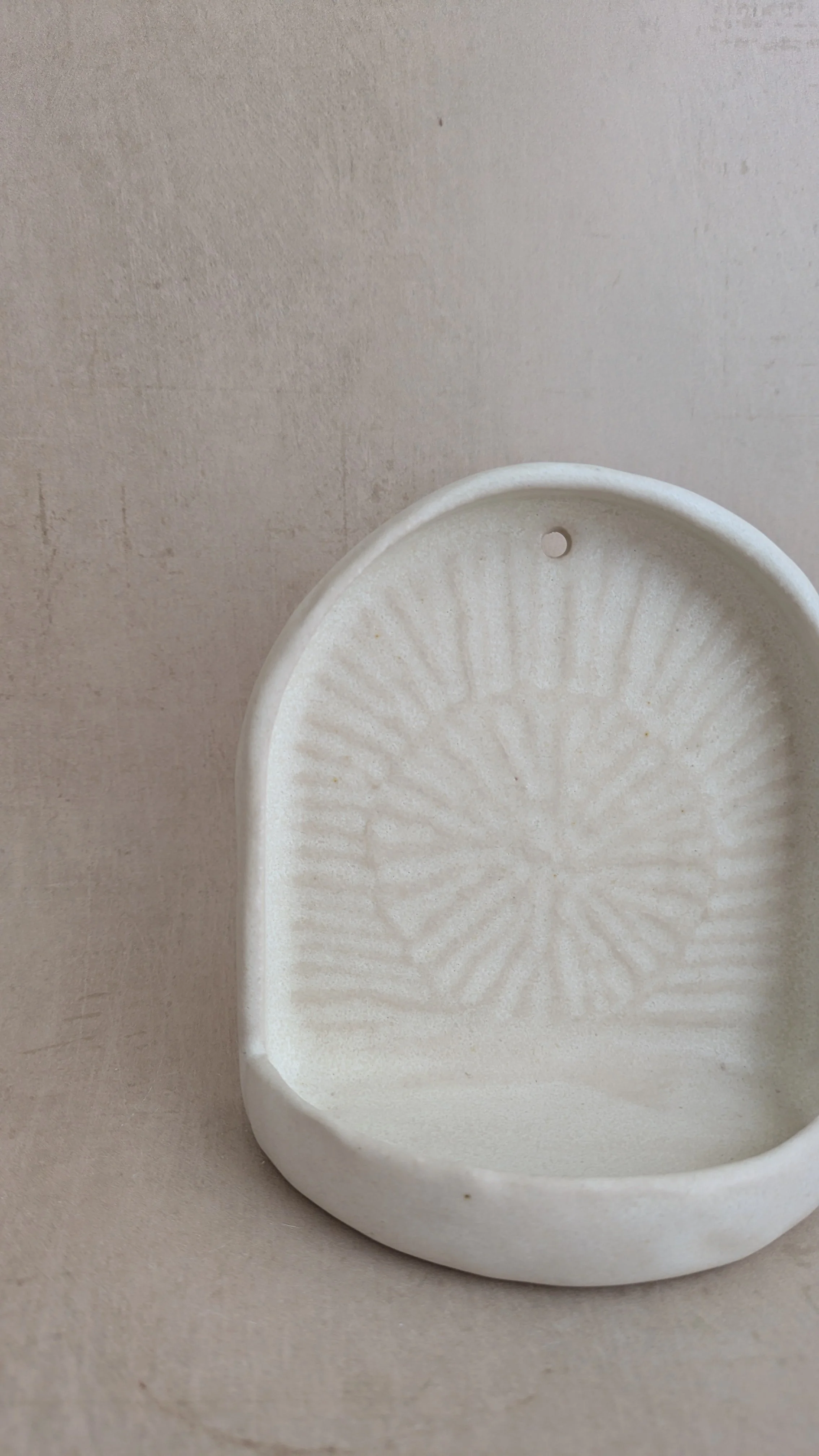 Close-up of cream ceramic wall sconce showing radial sunburst texture and hanging hole detail.