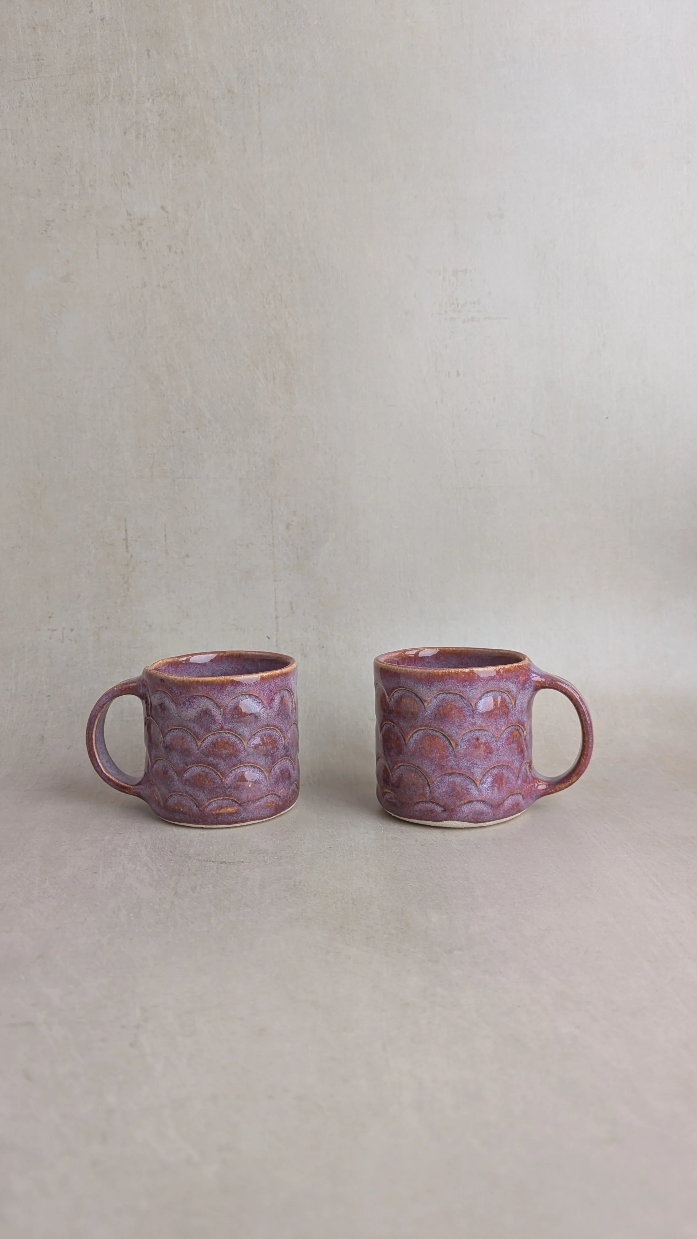 Two small purple mugs side by side, showing their rounded handles and textured scalloped design.