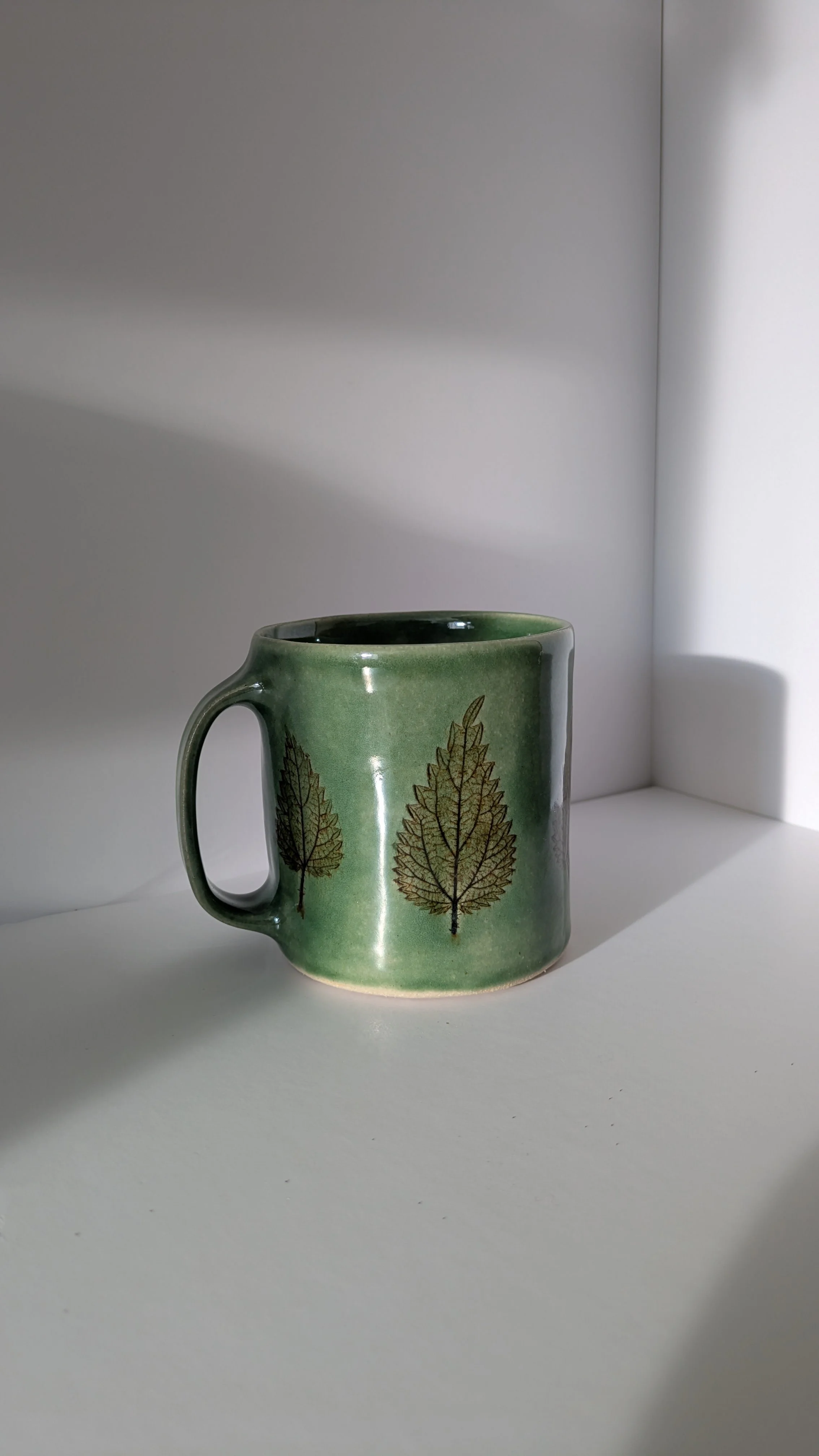 Single large nettle mug with green glaze and leaf motif, shown from an angled side view.