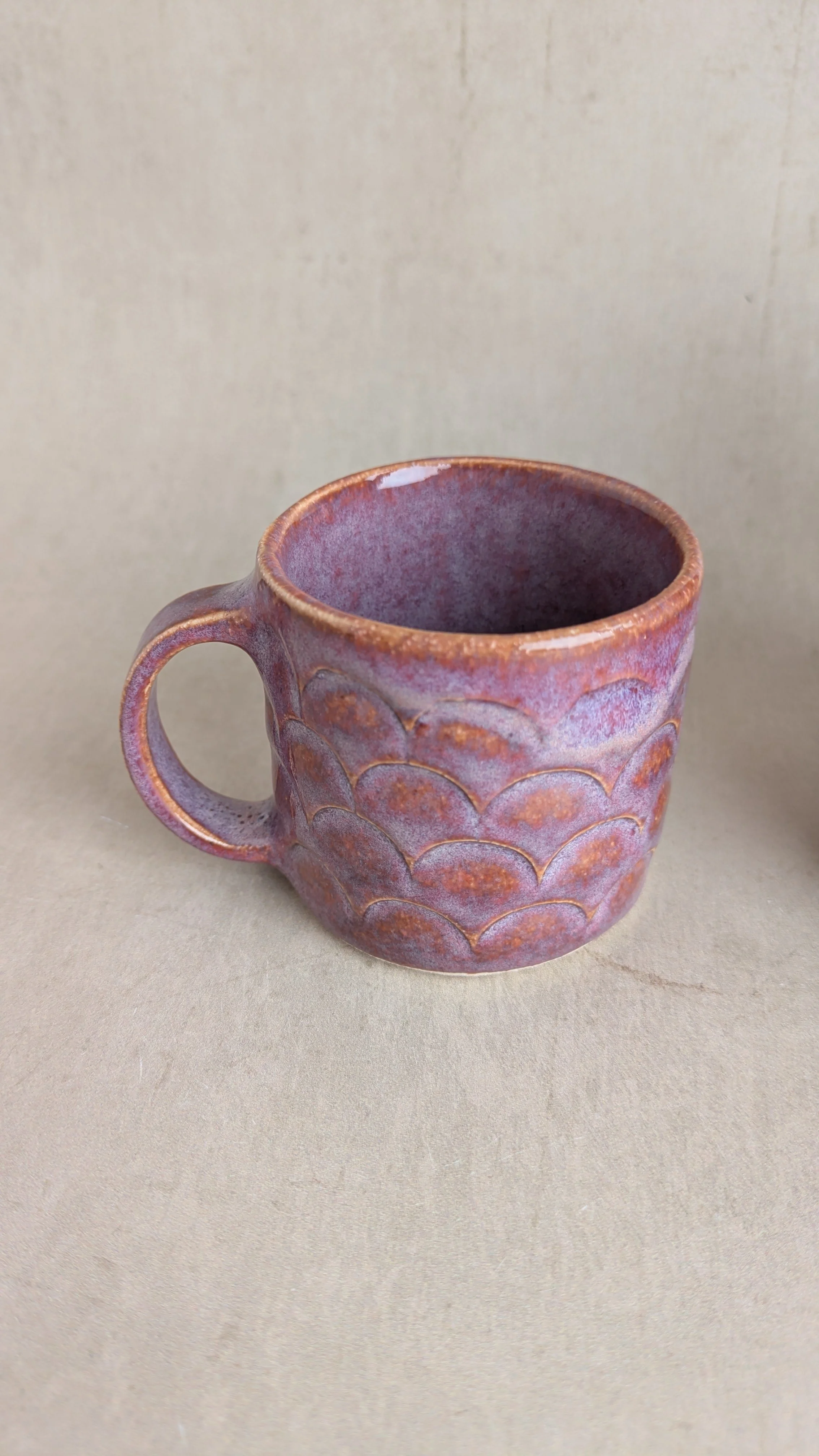 Small textured purple mug with scalloped pattern and warm reddish tones, on a neutral background.