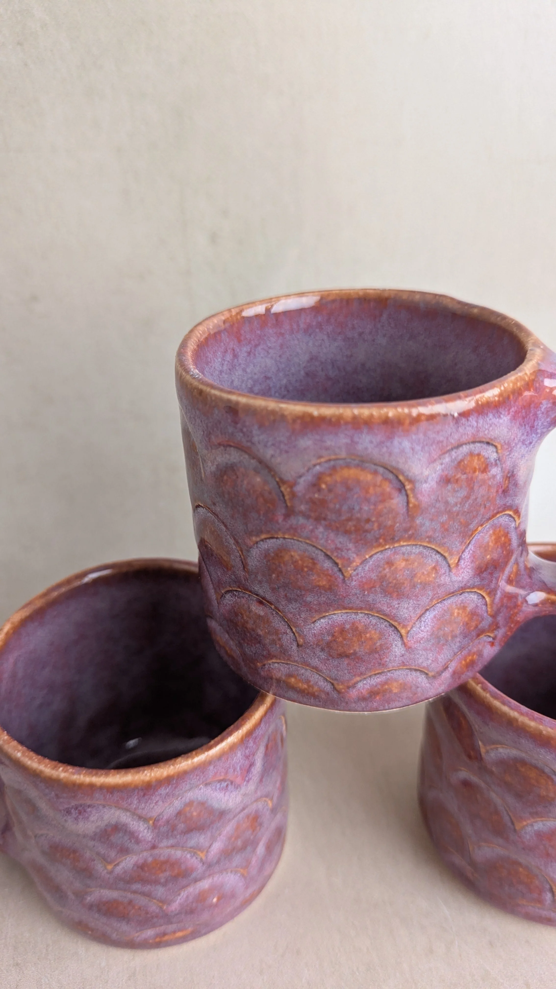 Close-up of small purple mugs highlighting the scalloped texture and variegated glaze finish.